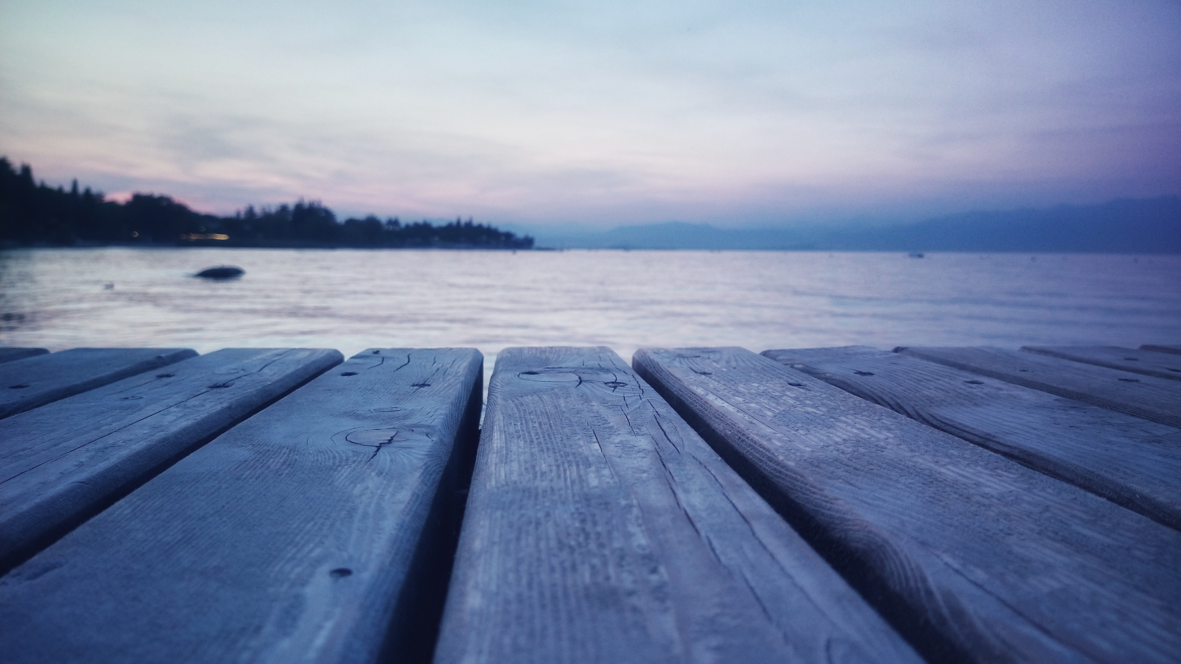 Wooden planks coloured slighly blue/purple in front of lake. In the distance outlines of a mountain chain can be made out