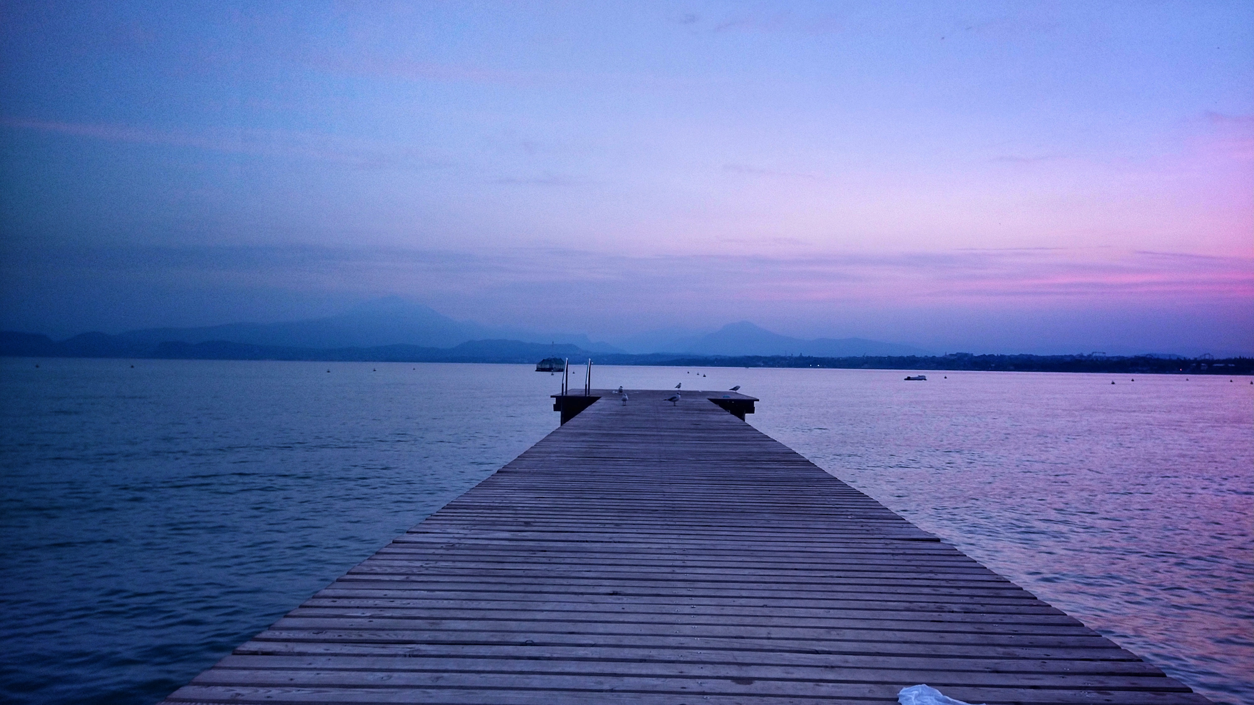 Wooden gangway leading out into the water. On the other side of the water, the outline of mountains, disappearing in the haze, can be made out