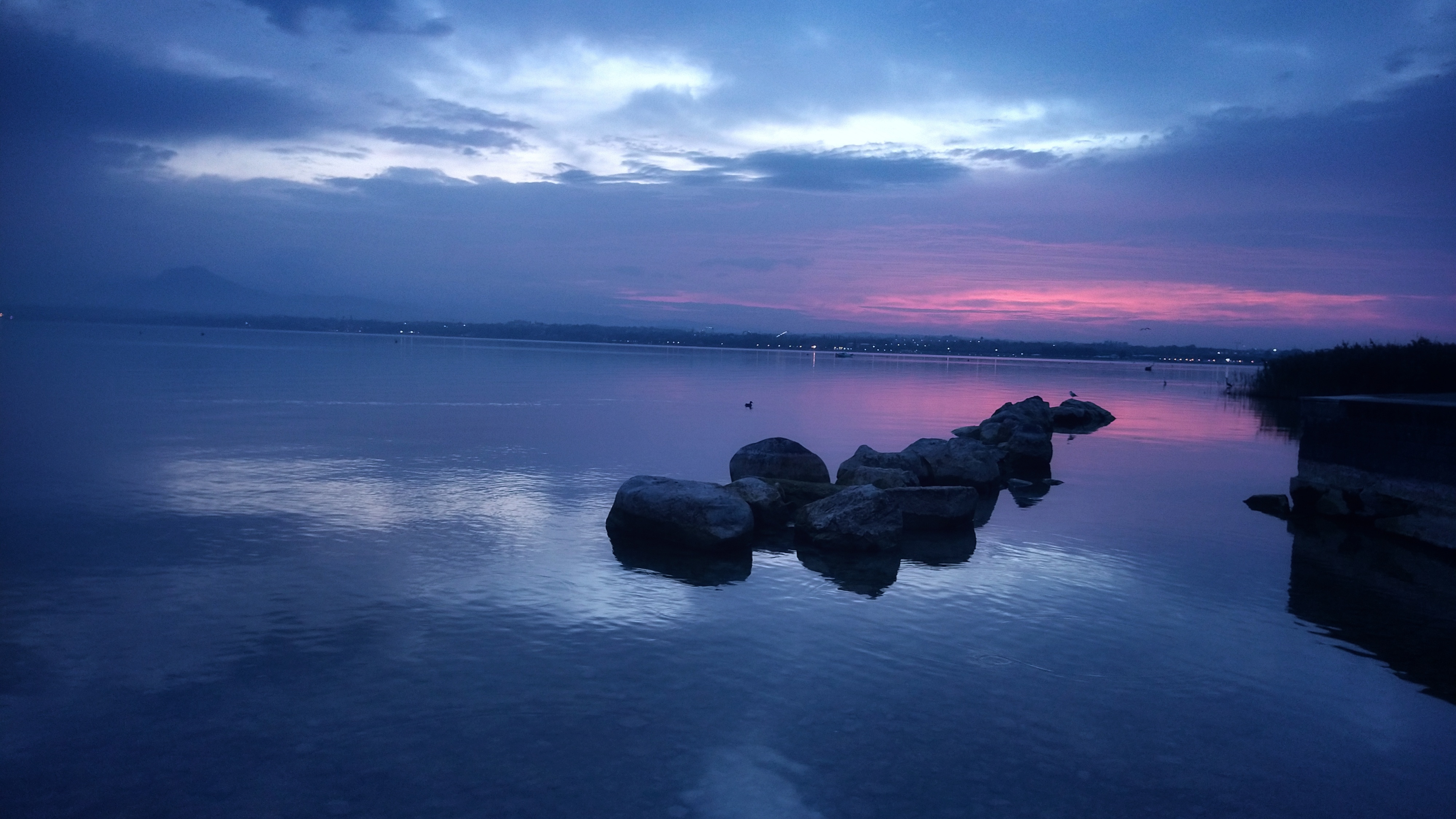 Group of rocks in the water. The sky is coloured a dark blue fading into a red hue