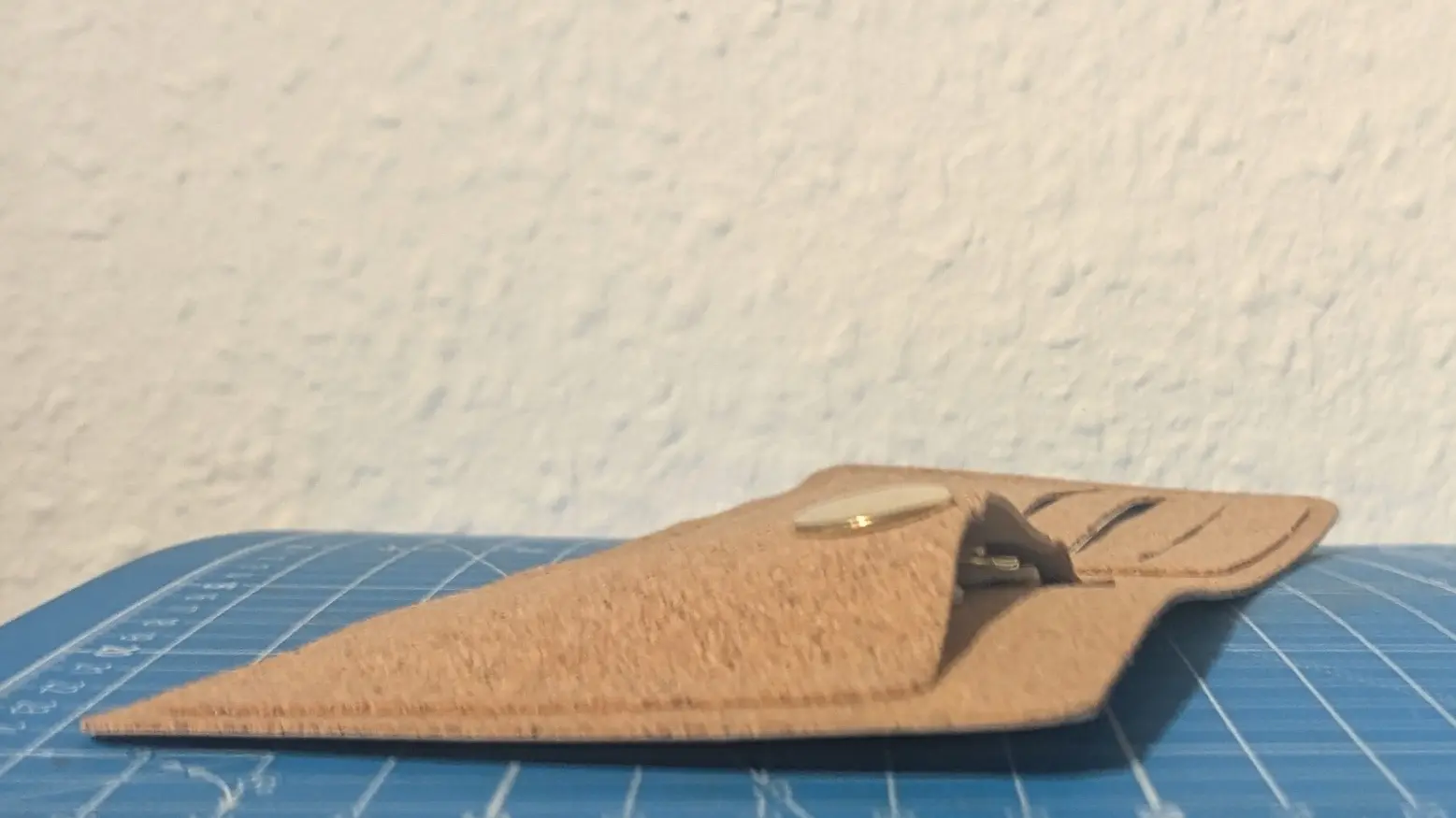 Sideways view of the cork wallet, showing the front of the coin pocket lifting about one centimeter from the inner sleeve.
One of the buttons used to close it is visible at the peak of the bend.