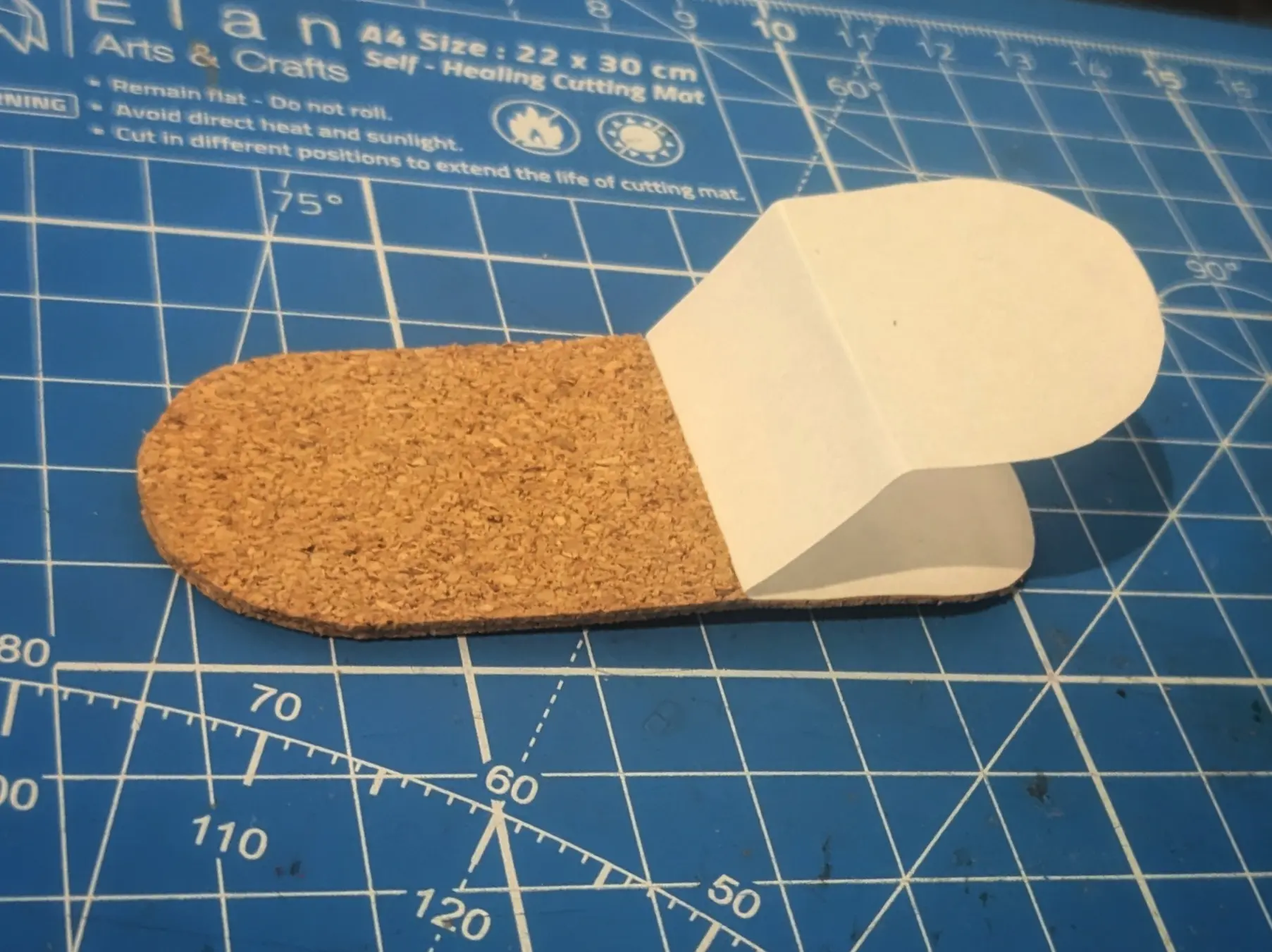 The latch: Rectangular cork piece with rounded corners.
A smaller piece has been glued on on the left-most two-thirds of it. The adhesive backing is still attached to the right third.