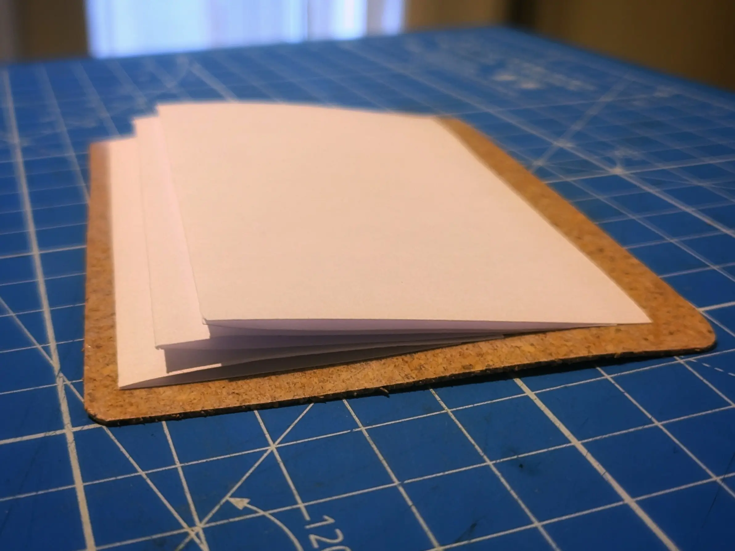 The cork rectangle with slots flipped upside down with the v-shaped pieces of paper glued to it, covering up the slots.
The paper flows from the slot towards the bottom and back up above the slot.
They form a sort of small staircase, as they each end slightly further up than the previous one.