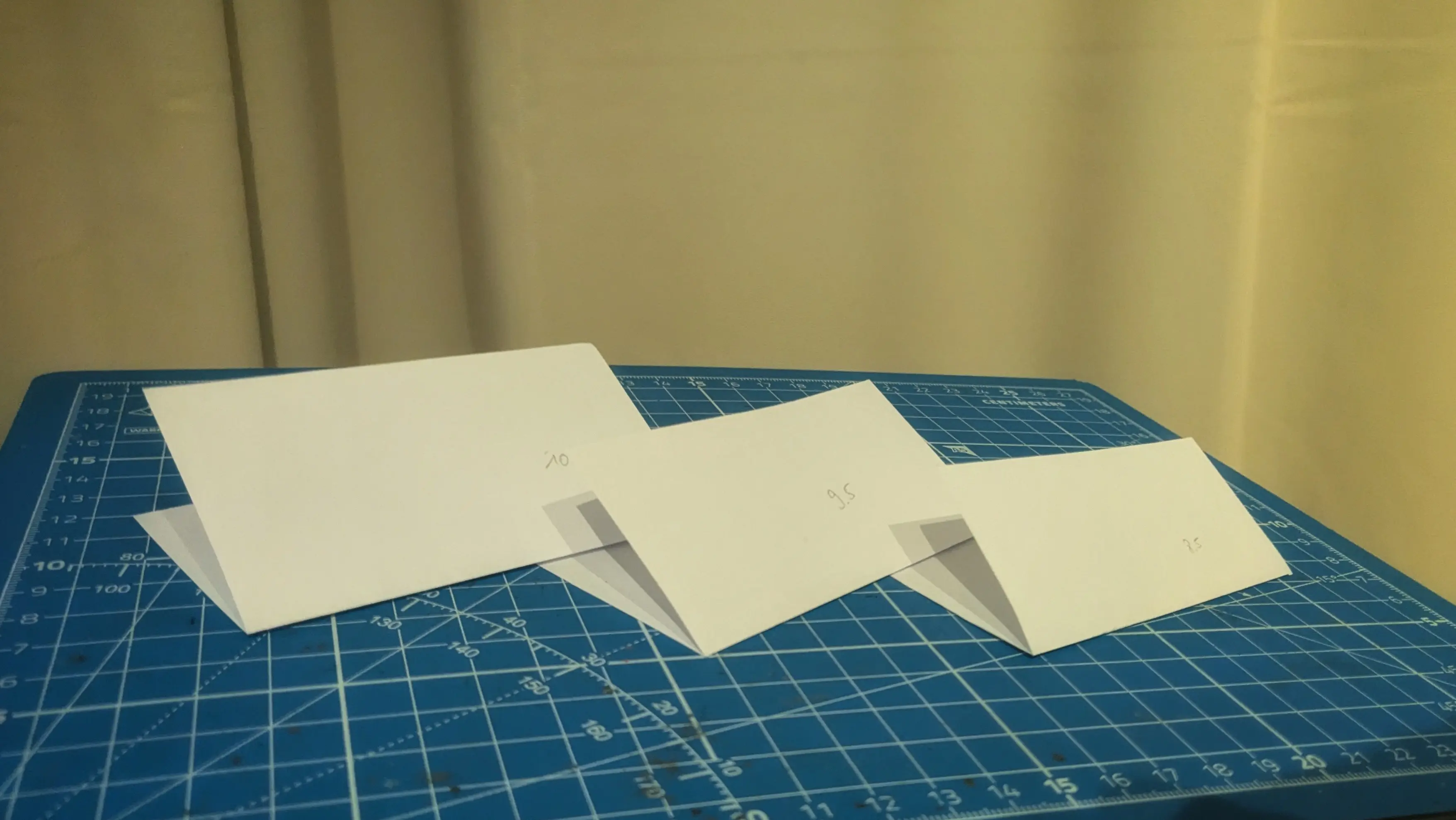 Three pieces of paper on a blue cutting mat, each folded into a V shape.