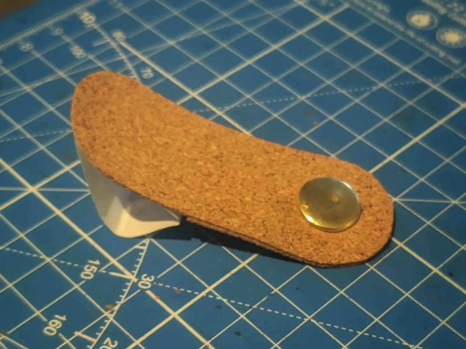 The latch piece placed with the adhesive facing down on a blue cutting mat.
A round golden button has been added on one side.