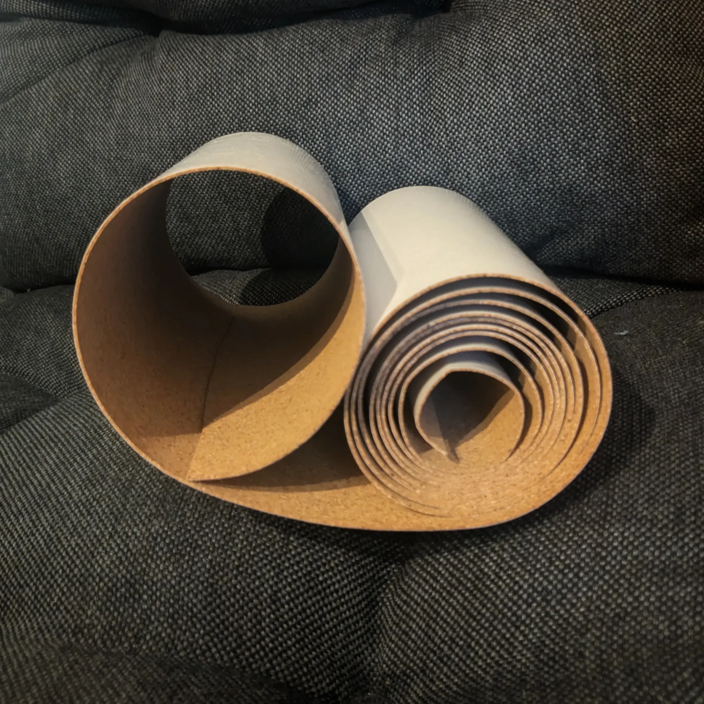 Curled up roll of thin cork with an adhesive backing placed on a gray pillow