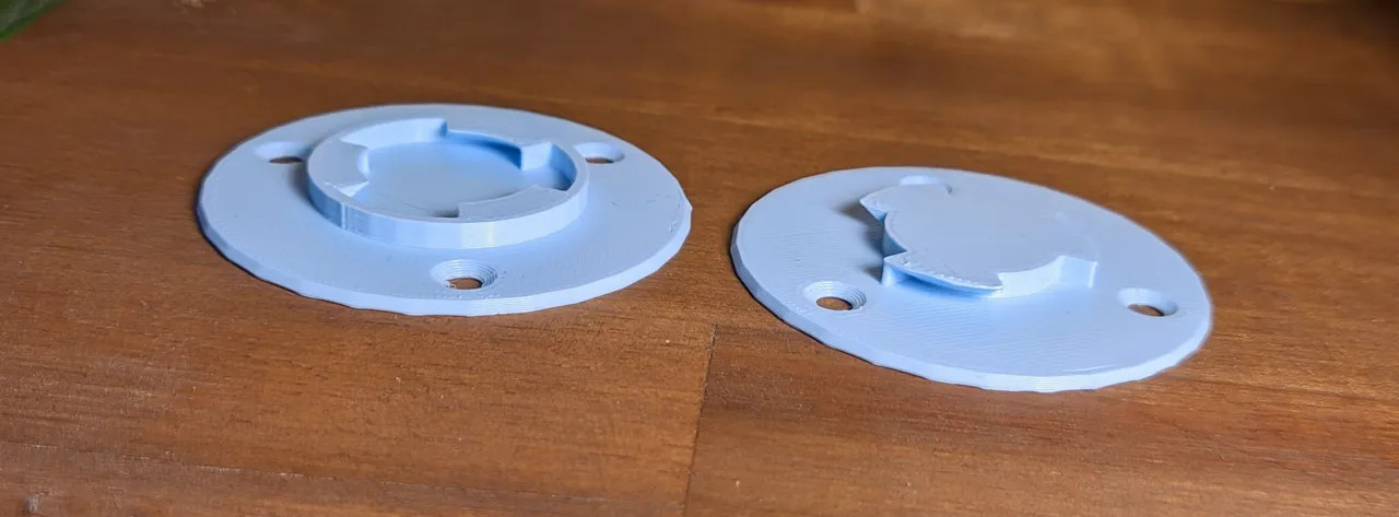 Two 3D printed models sitting on a desk. The left one has circle with hooks on the inside. The right one has a cylinder in the middle with hooks on the outside. The positions of the hooks line up, allowing the parts to fit together