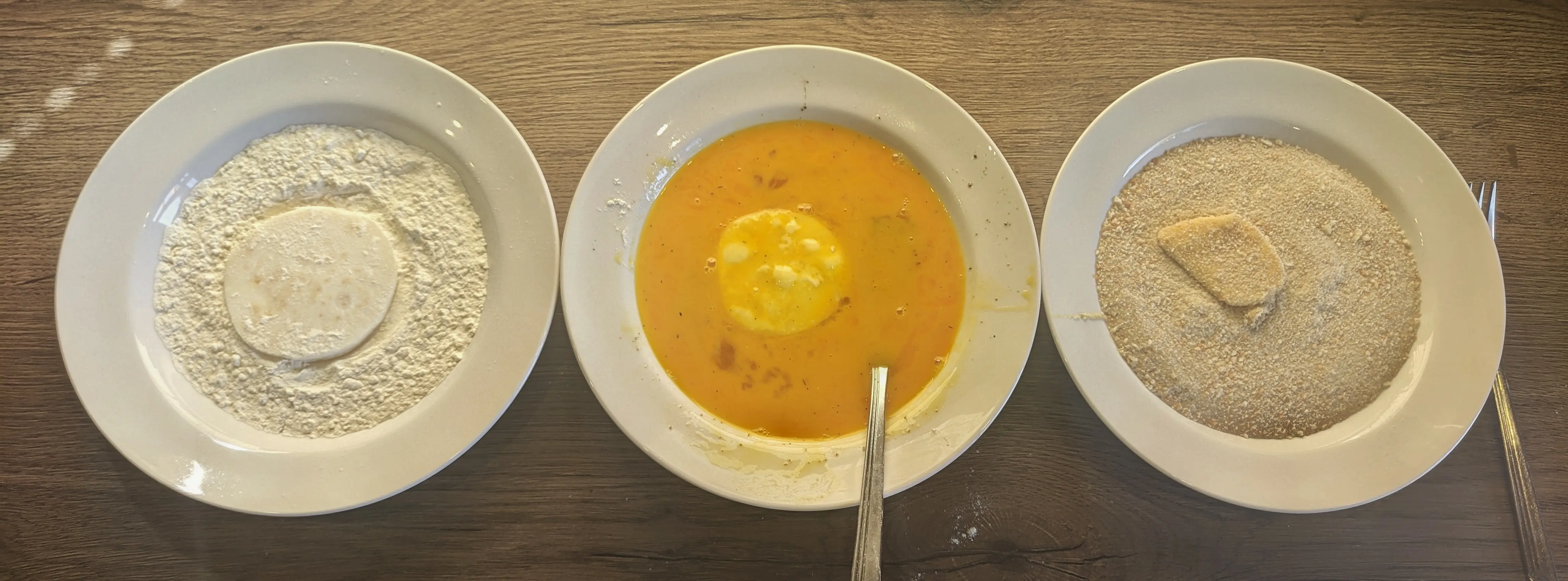 The same three plates in a line, but the eggs in the middle one have been beaten together, mixing in the salt and pepper.
All the plates also contain a celeriac piece each, showing them coated in the appropriate ingredients.