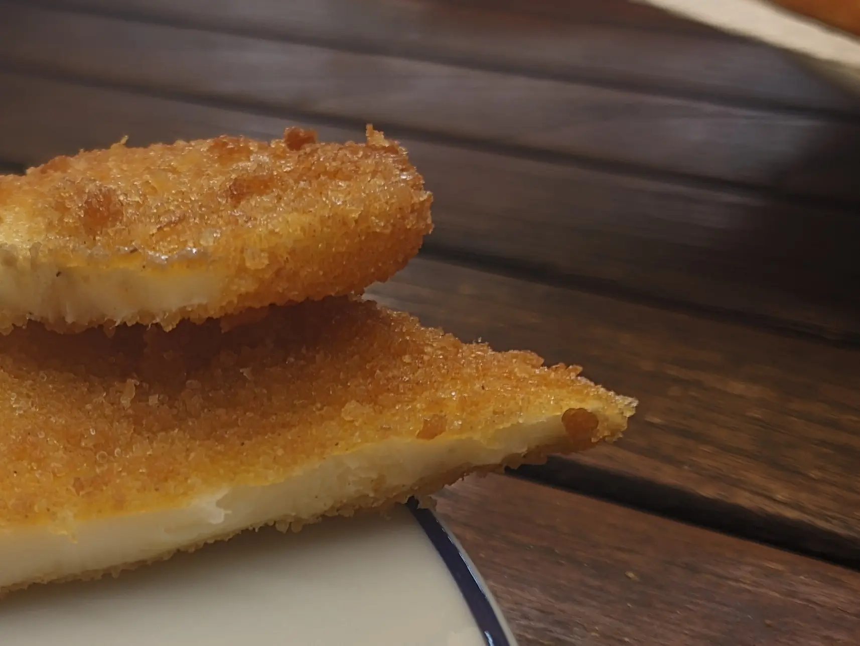 Close-up of a celeriac slice cut in half, showing the white but slightly transparent inside and the crispy and uneven texture of the breading.