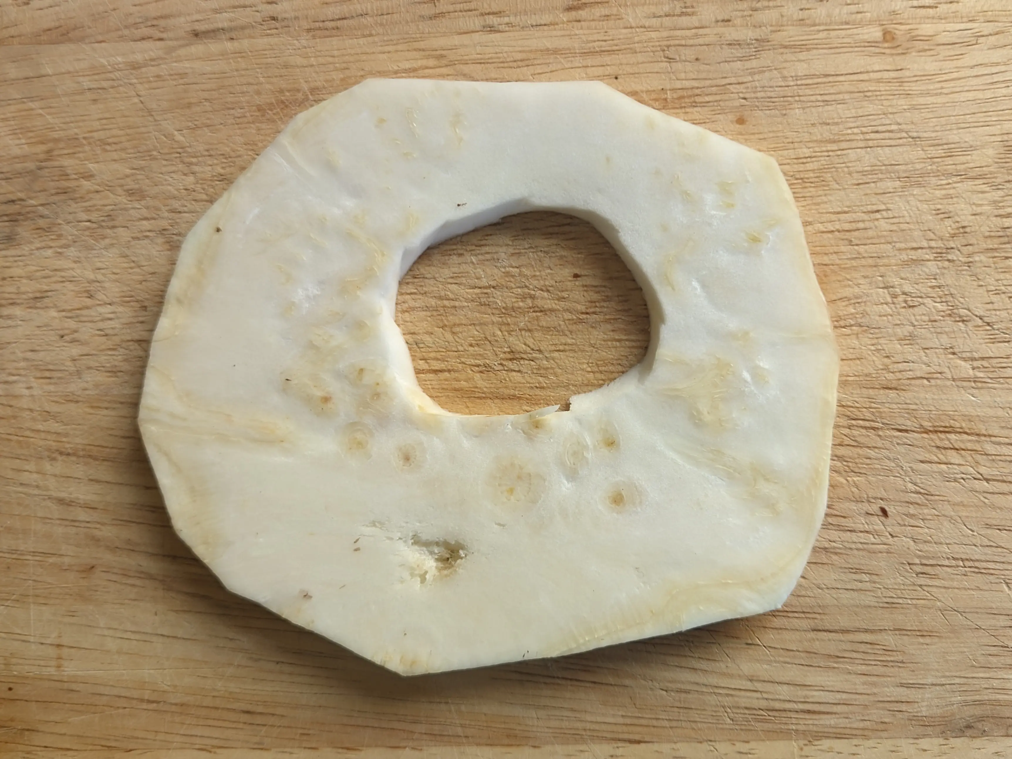 A single large celeriac slice on a cutting board. A uniform hole has been cut in the middle to even out the natural air pocket.