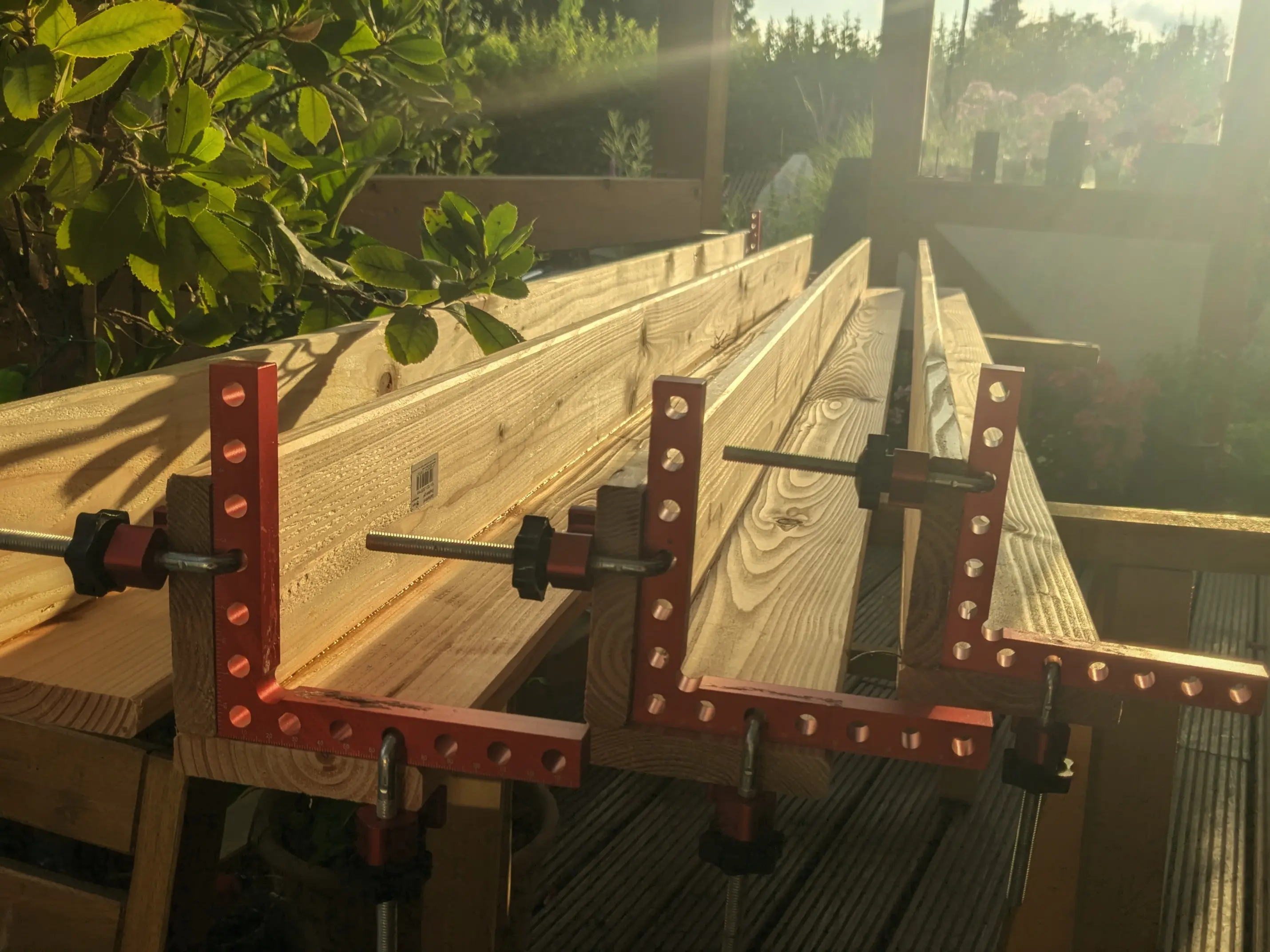 Four long L shaped wooden beam assemblies on supports.
Some of them are fixed to right angle brackets.
A plant is spreading its leaves over the left most beam assembly.
The sun set highlights the colour of the Douglas fir in a nice warm colour. Four long L shaped wooden beam assemblies on supports.
Some of them are fixed to right angle brackets.
A plant is spreading its leaves over the left most beam assembly.
The sun set highlights the colour of the Douglas fir in a nice warm colour.