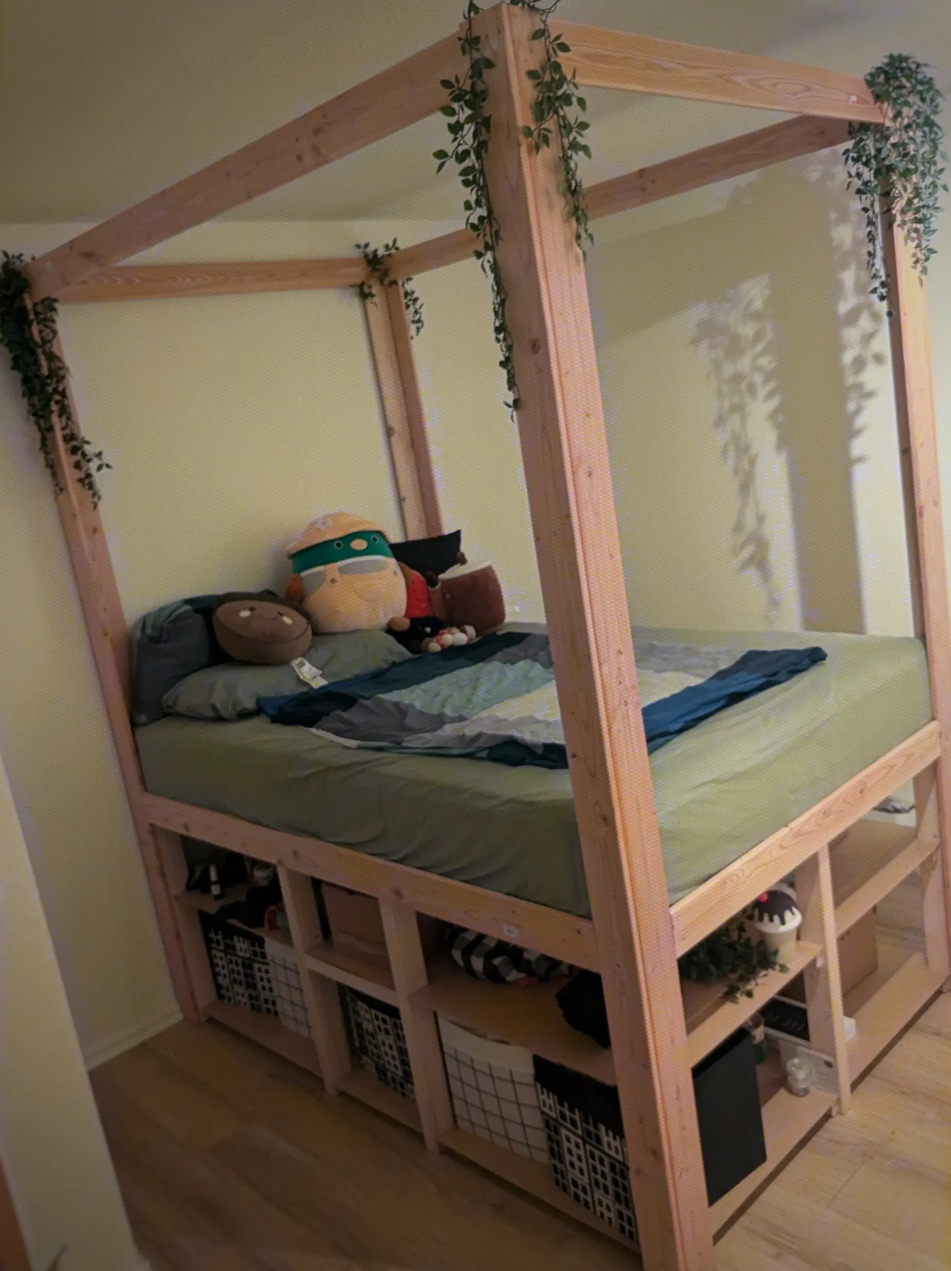 Fully assembled bed with a mattress on it.
The shelves have been filled with boxes and somewhat chaotic boxes and items of clothing.
A couple of plushies are sitting on the bed, probably claiming it as theirs.
Green vines can be seen hanging from the canopy structure. Fully assembled bed with a mattress on it.
The shelves have been filled with boxes and somewhat chaotic boxes and items of clothing.
A couple of plushies are sitting on the bed, probably claiming it as theirs.
Green vines can be seen hanging from the canopy structure.