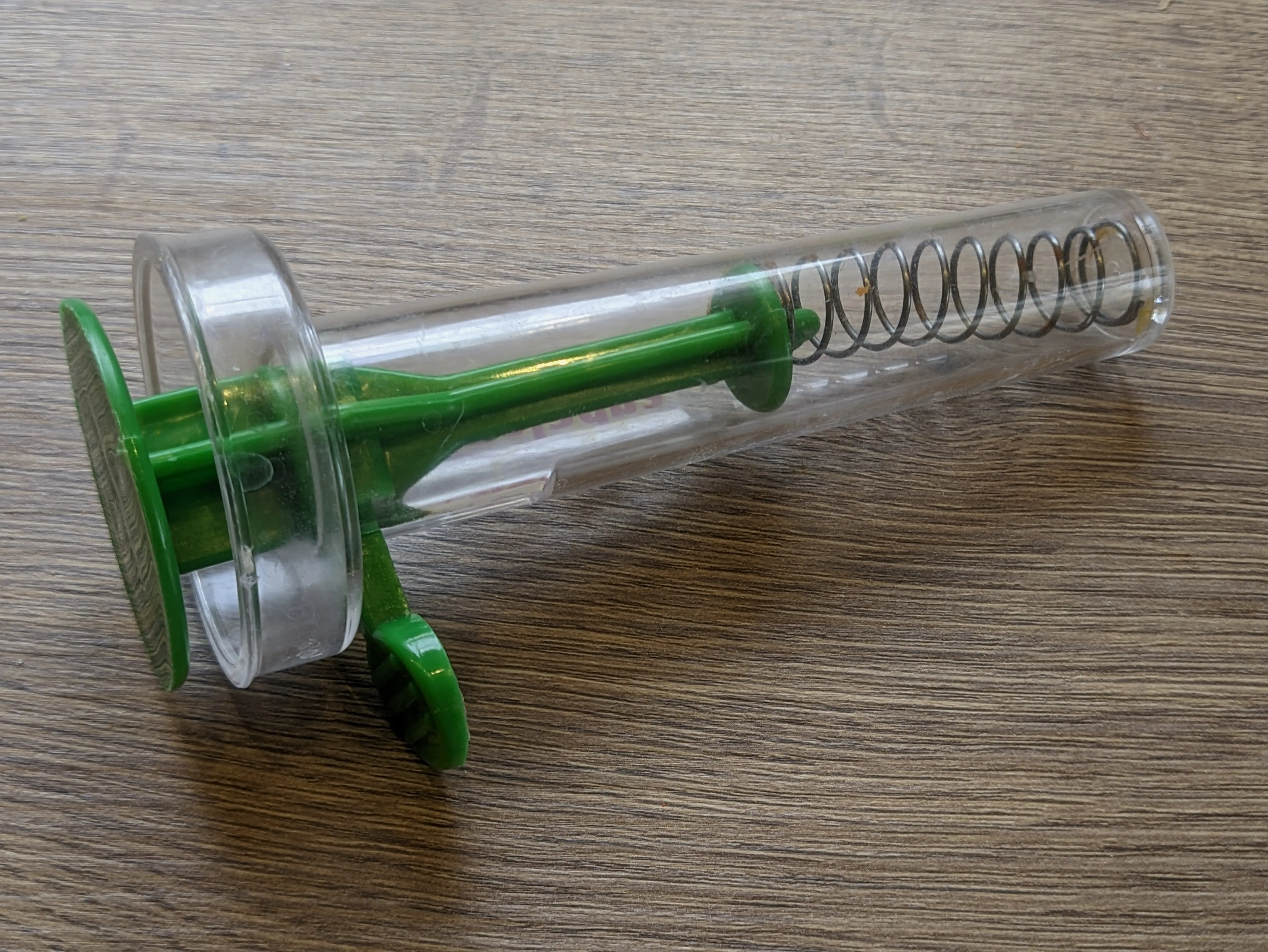 A transparent falafel press, showing the level which can be used to compress a spring to pull back the main cylinder shaped platform