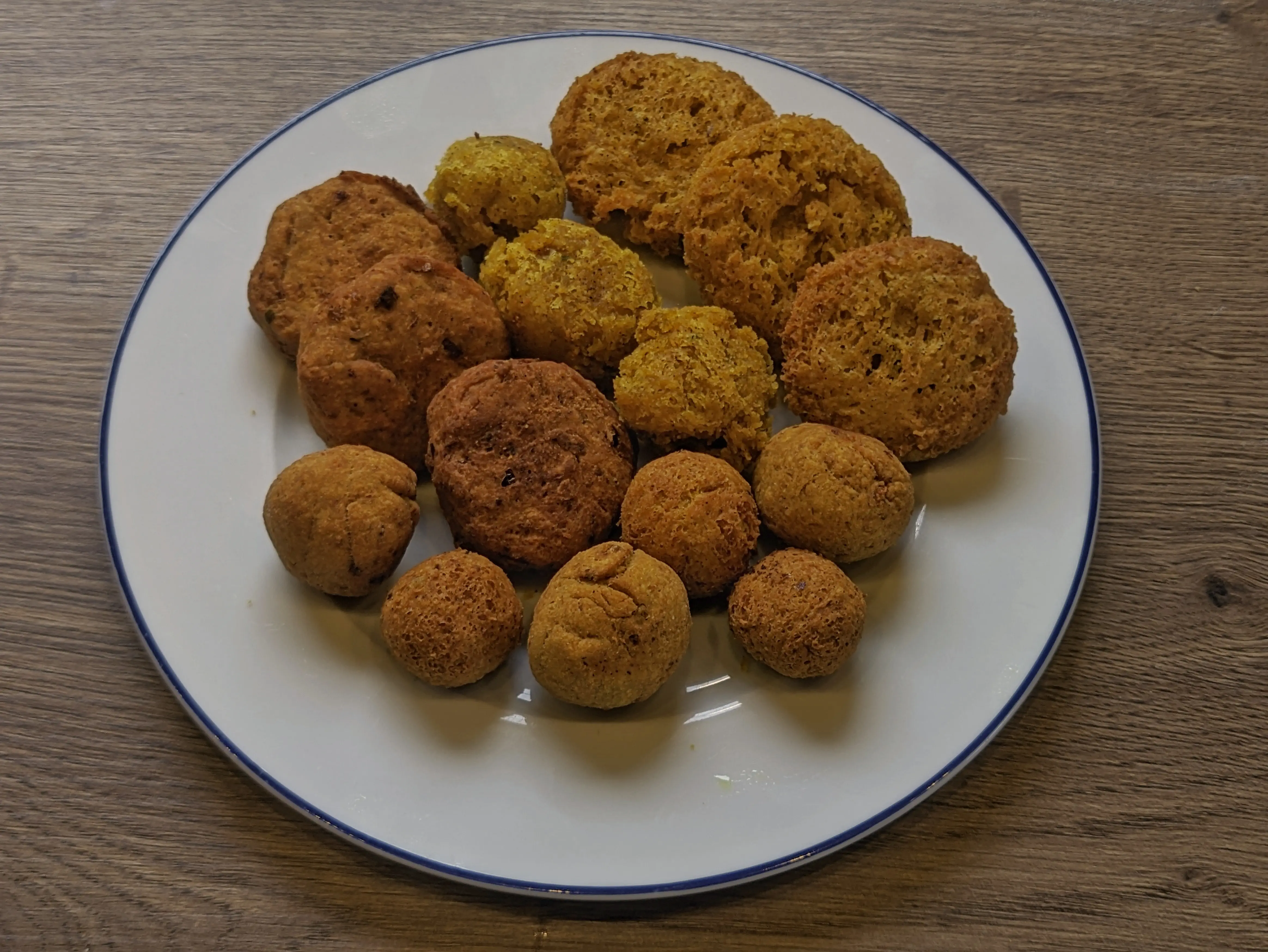 Different shapes of falafel on a small plate. They look brown and crispy on the outside, almost like meatballs.