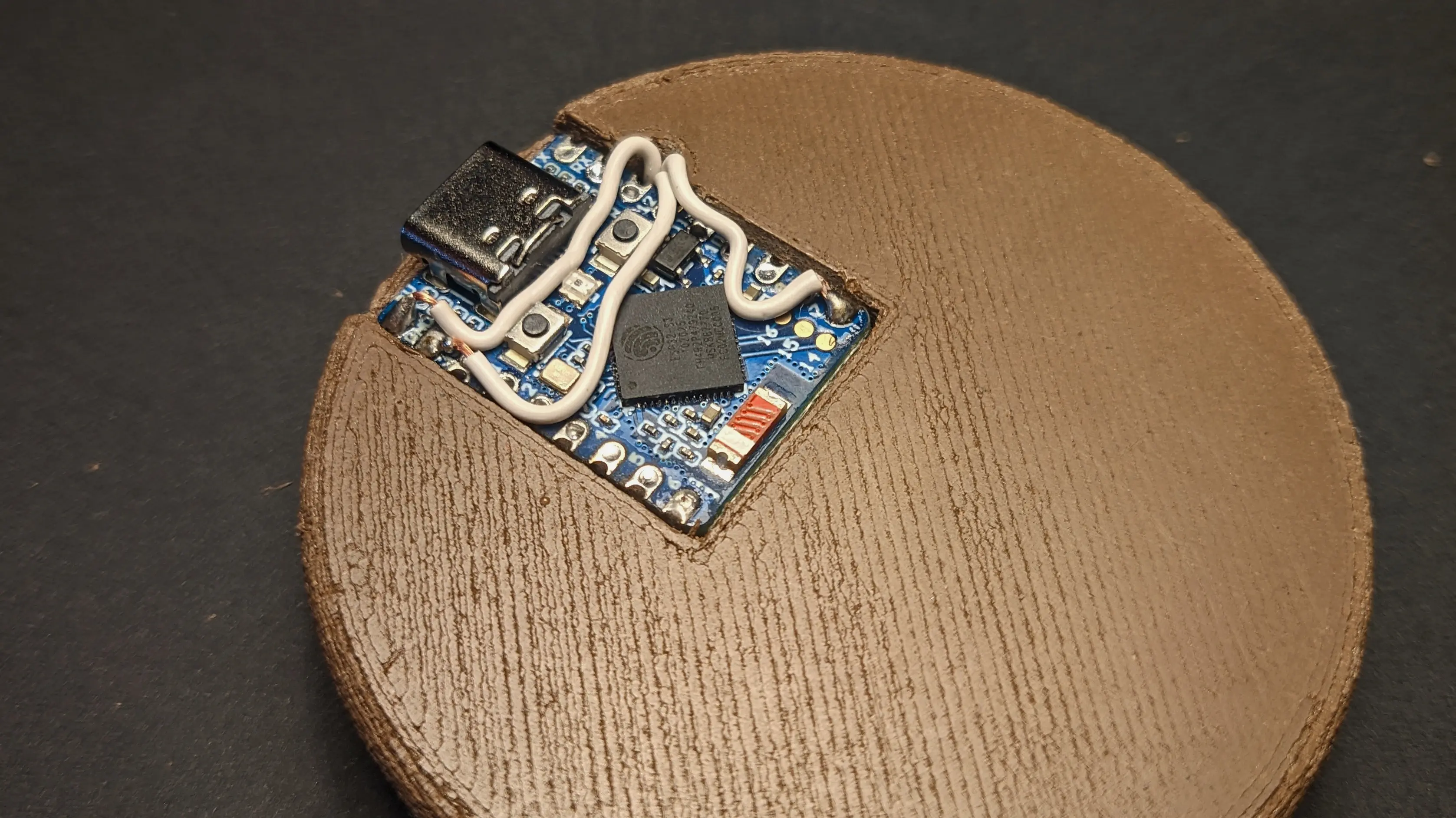 A small blue circuit board has been placed in the rectangular recess on the bottom piece.
Three wires are soldered to its pins, and the USB-C port is sticking out the side.