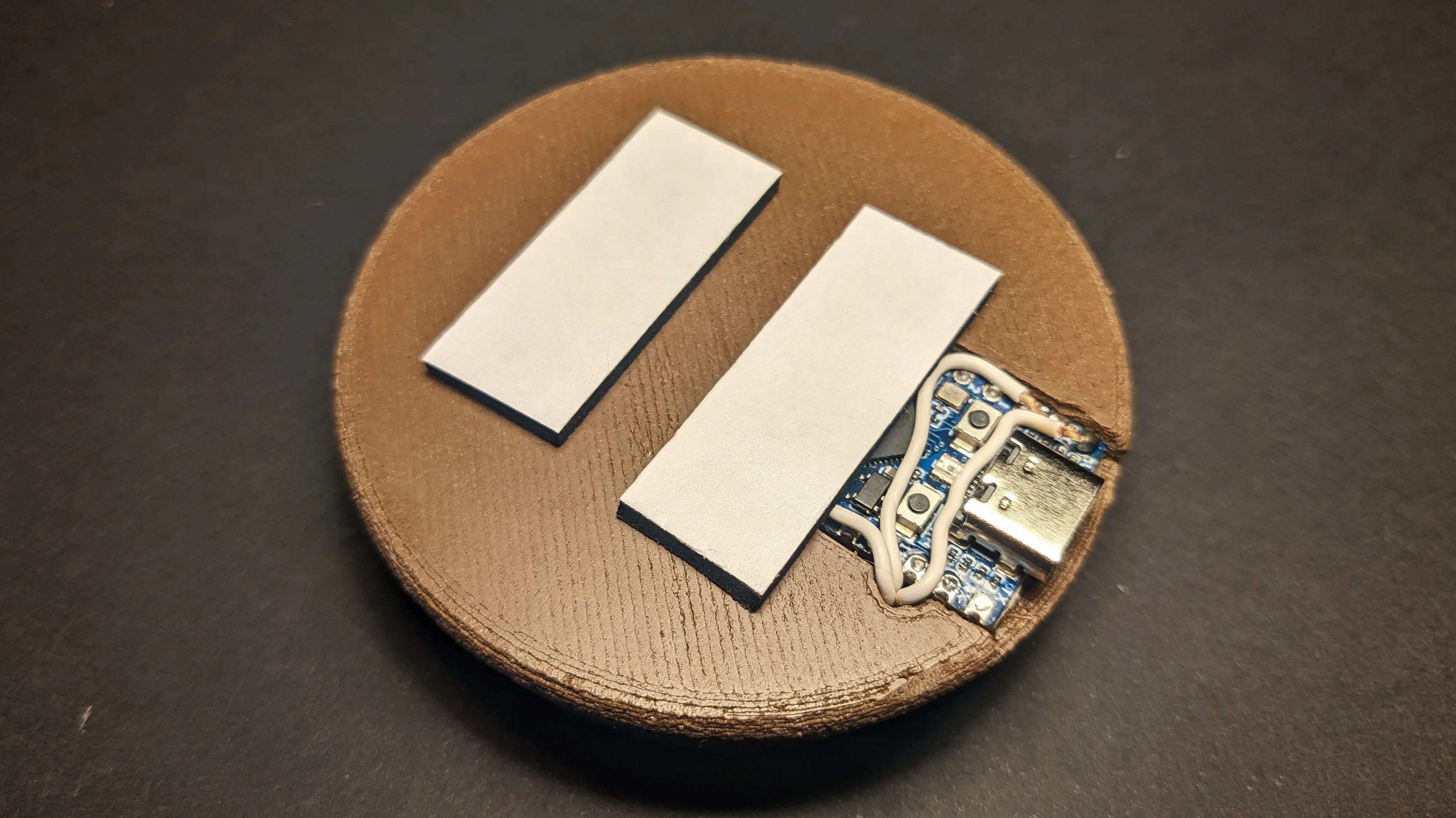 The assembled base, but flipped upside down, showing two black foam adhesive strips stuck to it.
One is partially obscuring the ESP. The strips still have their backing paper on them.