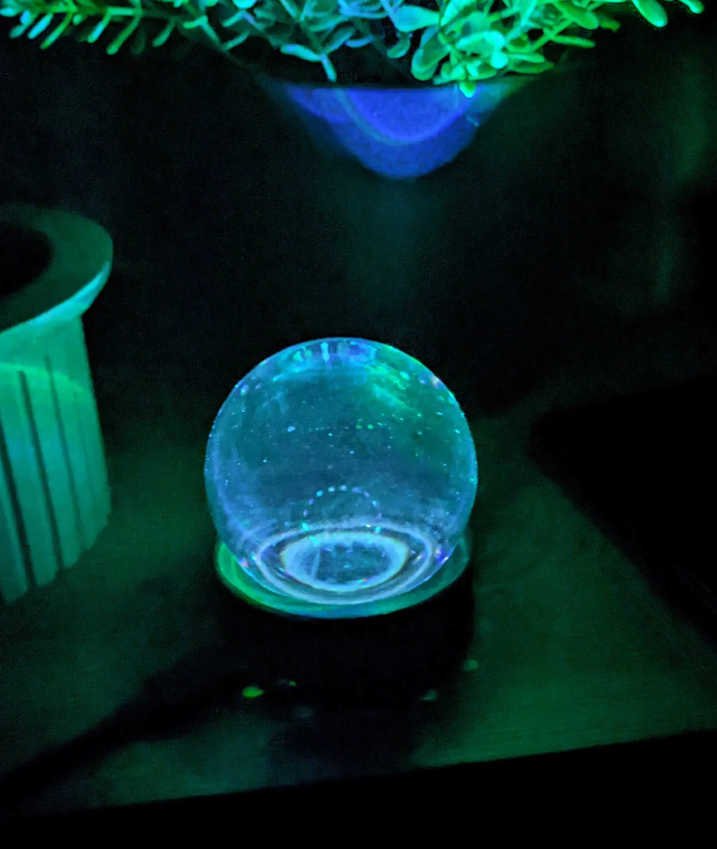 GlowOrb sitting on the same nightstand, with a second planter visible.
The ball is now glowing blue and green and reflecting light on both planters.