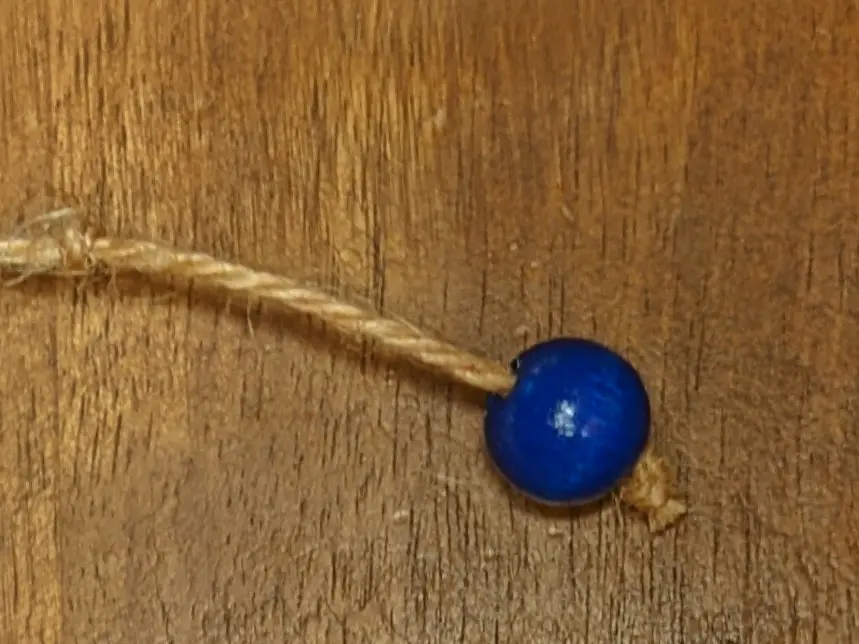 A section of twine, with a blue wooden bead on one end, followed by a knot and a secondary knot roughly 4 cm from the end.