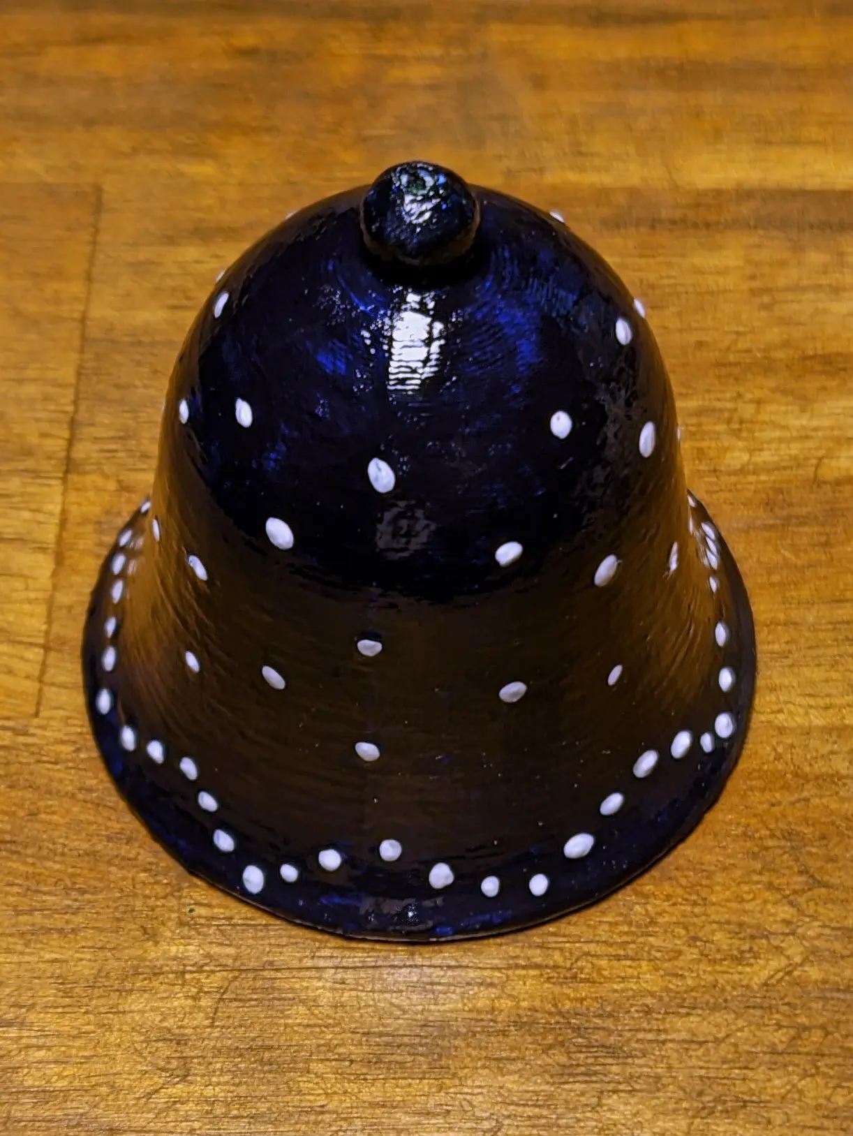 Completely painted bell placed on the desk. The glossy topcoat hightlights the blue and white paint and causes the light to reflect off the bell.