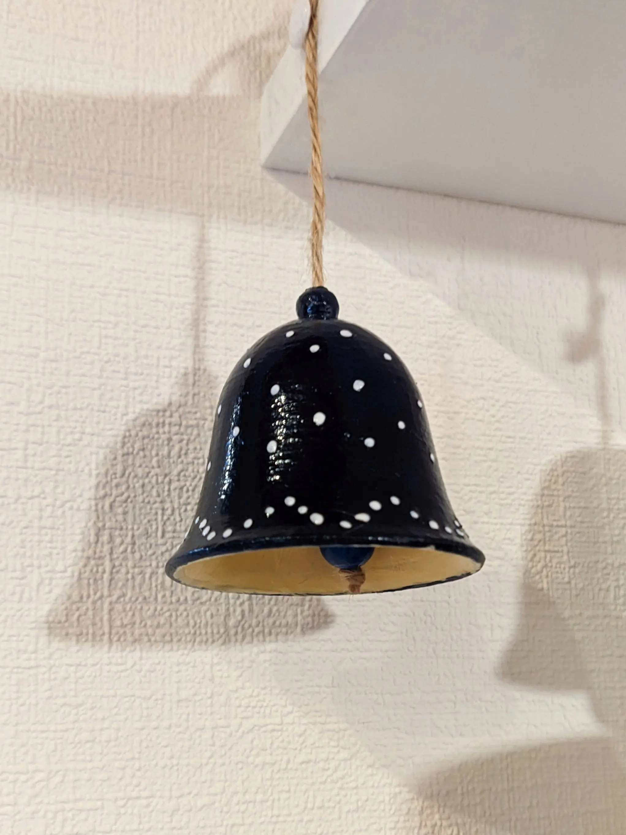 The finished bell hung from a shelf, casting a shadow on the wall. Both the shiny blue outside with white bumps and the ochre inside are visible. Some small imperfections in the paint are visible along the seam where the two colors meet.