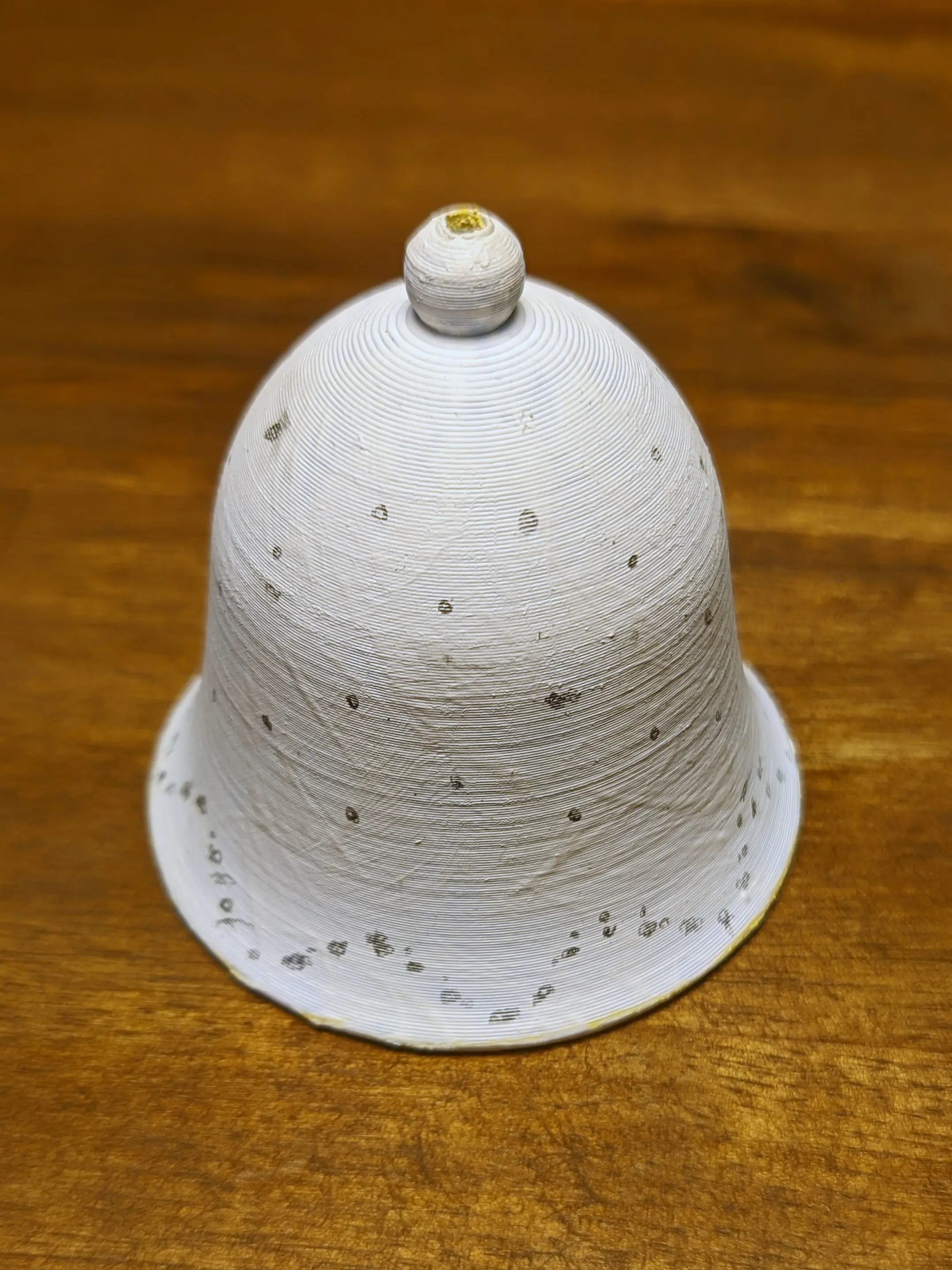 White bell with pencil markings on it. Some marks have been crossed out. The markings form a wave pattern on the flared-out section. On the upper section the markings alternate between three and two points.