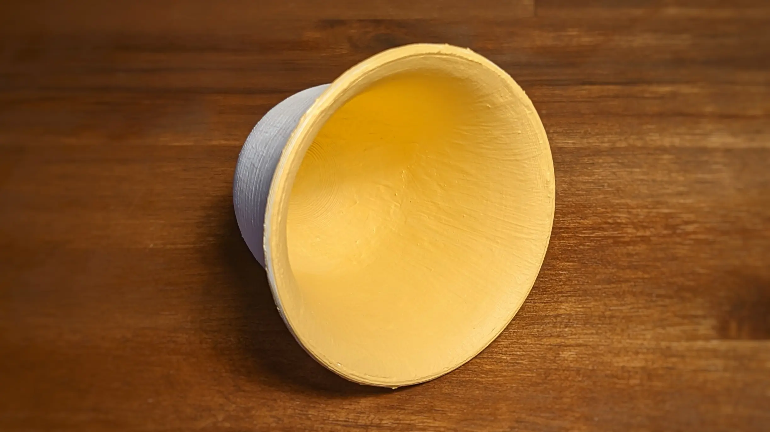 The bell has been placed on its side with the inside facing towards the camera. The outside is white, and the inside has been painted an intense yellow/ochre color.