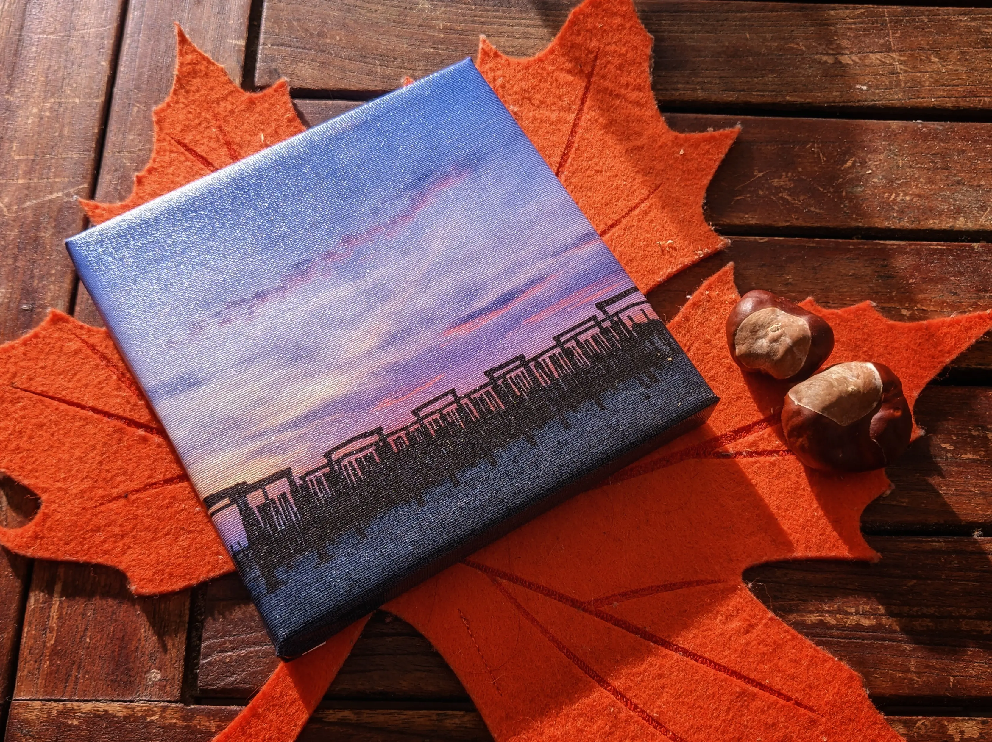 The completely wrapped canvas frame placed on an orange leaf-shaped table mat, next to some chestnuts.
The printed image has vivid colors with deep red and orange hues.
The canvas texture can be made out on the entire frame, giving it a really professional look.
