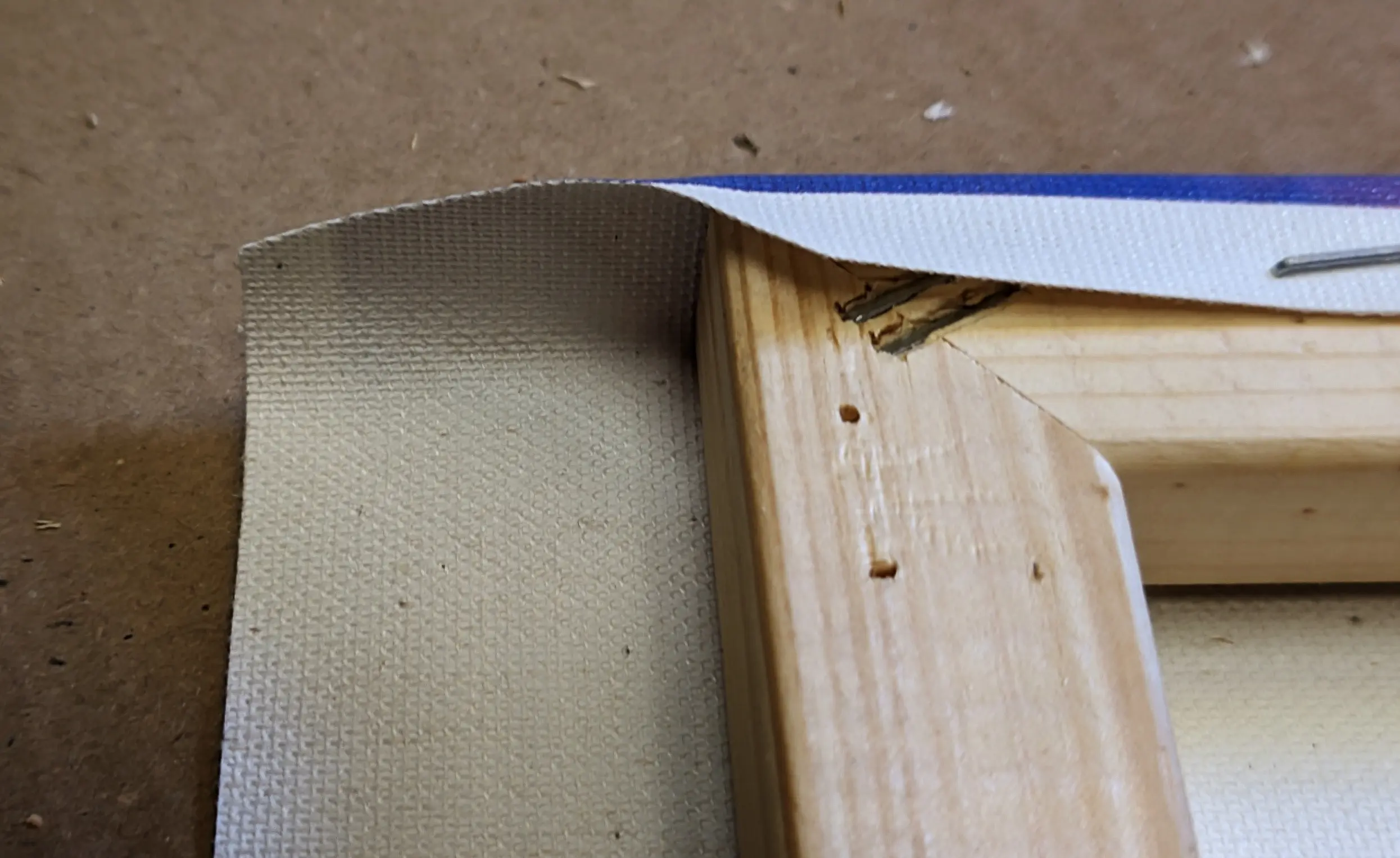 The corner of the canvas sheet cut off at a roughly 30-degree angle, connecting the midpoint of the extending side canvas piece with the top where the sheet has been fixed to the frame.