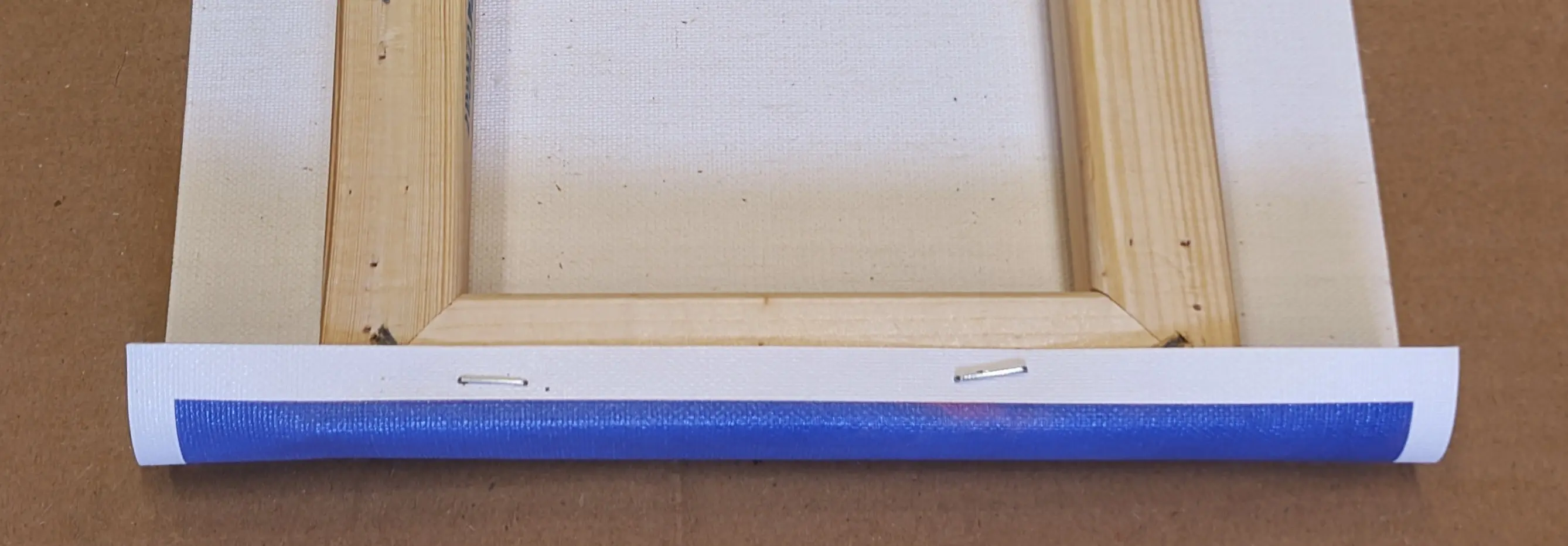 One side of the canvas sheet folded over to the back of the frame and stapled in place in two places.
Parts of the photo are visible on the now exposed front of the canvas sheet on the side of the frame.