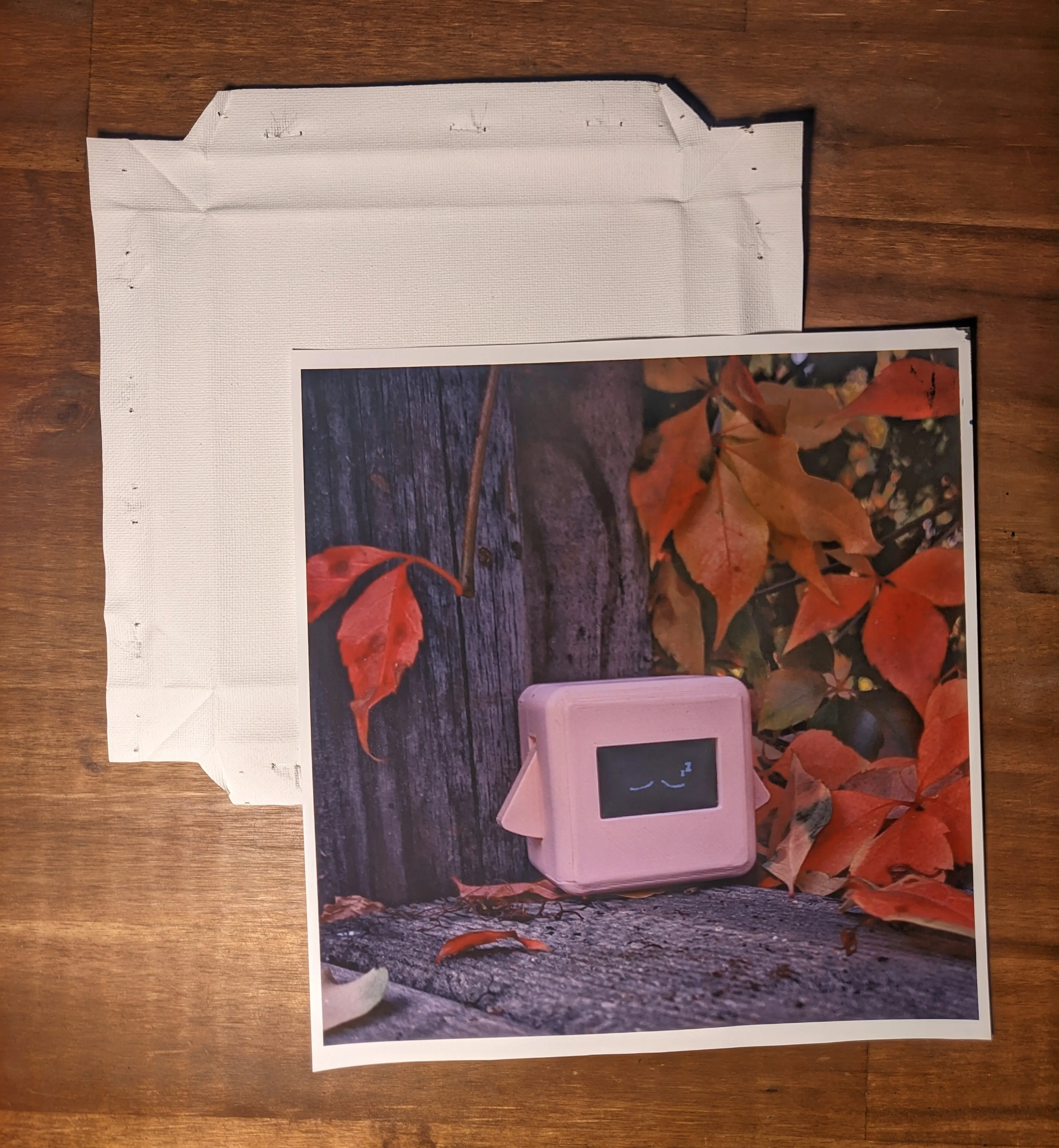 A printed square photo of a toy block on wooden boards with leaves placed slightly offset on top of the flattened canvas sheet.
The printed image has deep colors and especially the leaves have a vivid orange-brown hue.