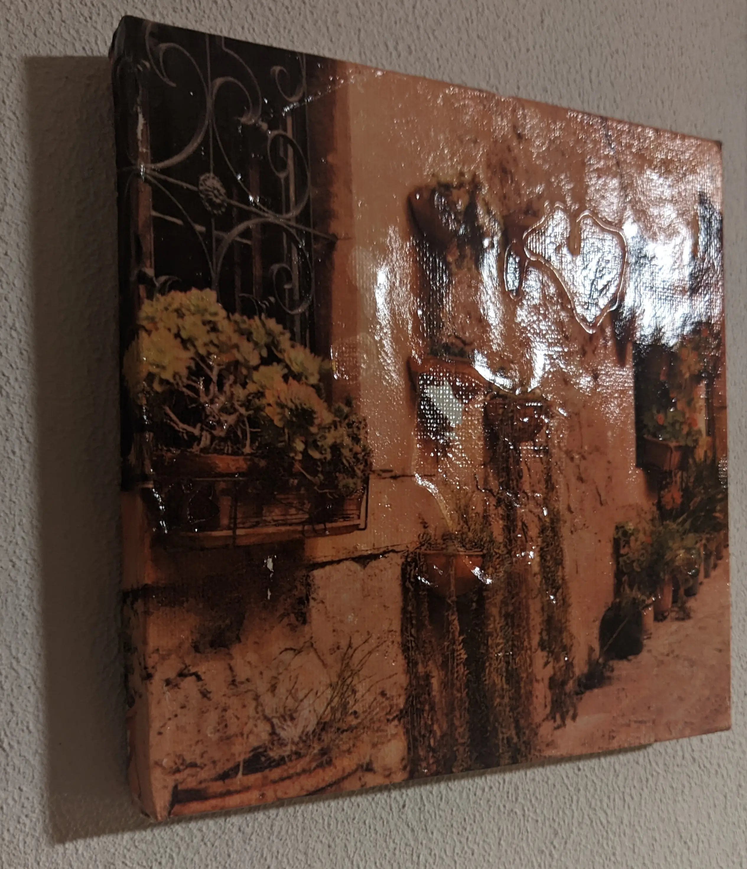 Canvas with a photo of a wall with flowerpots. The canvas has visible indented areas, where there wasn&rsquo;t enough glue and areas where there was too much. The paint is missing in one area. A smooth glossy finish has been applied on top to prevent paint from chipping away.