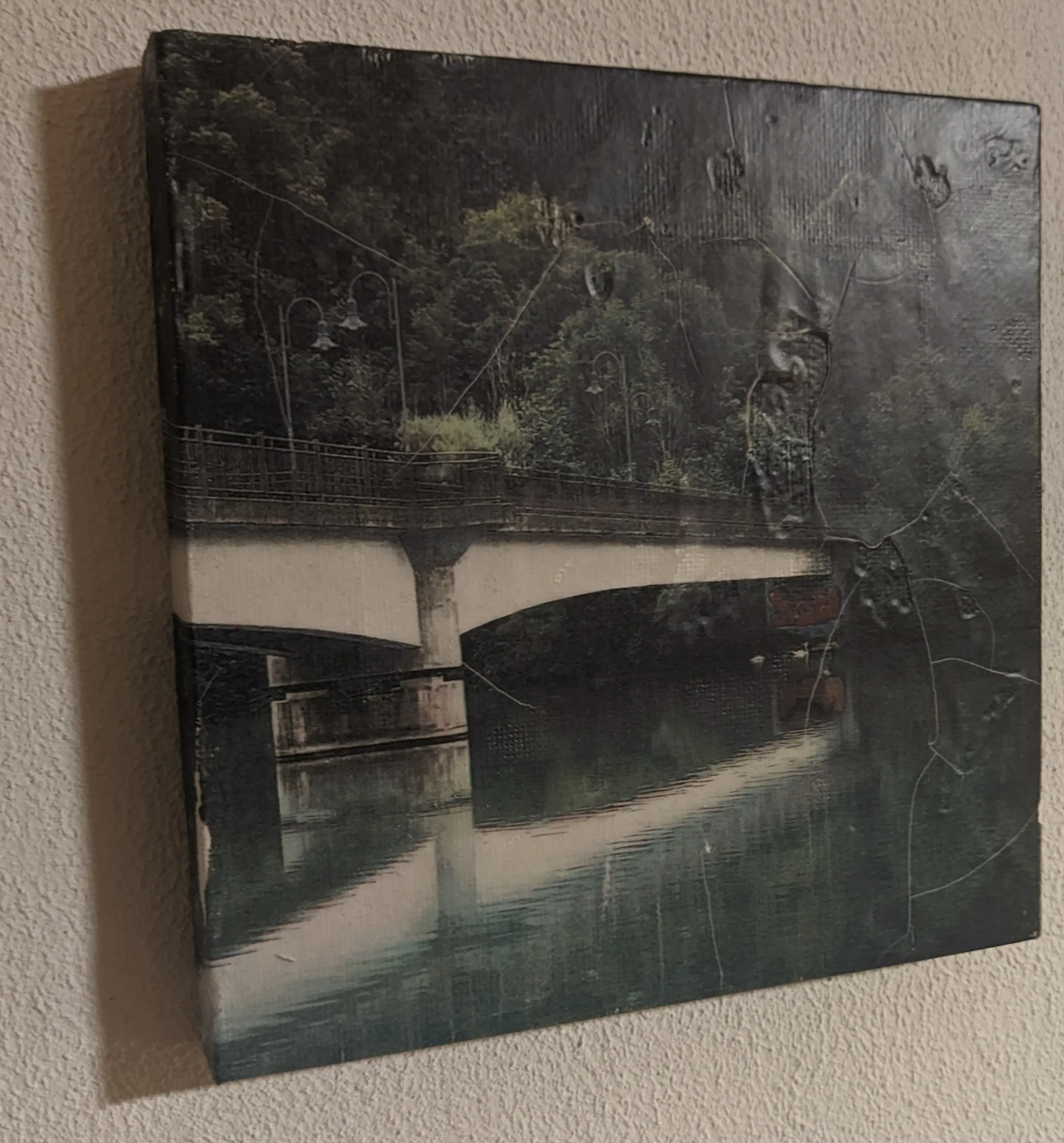 Canvas with a photo of a bridge across a river. The canvas has a matte finish to it, making it look premium but not like it is a piece of canvas. The matte finish has chipped in a bunch of places, giving it a spiderweb-like appearance.