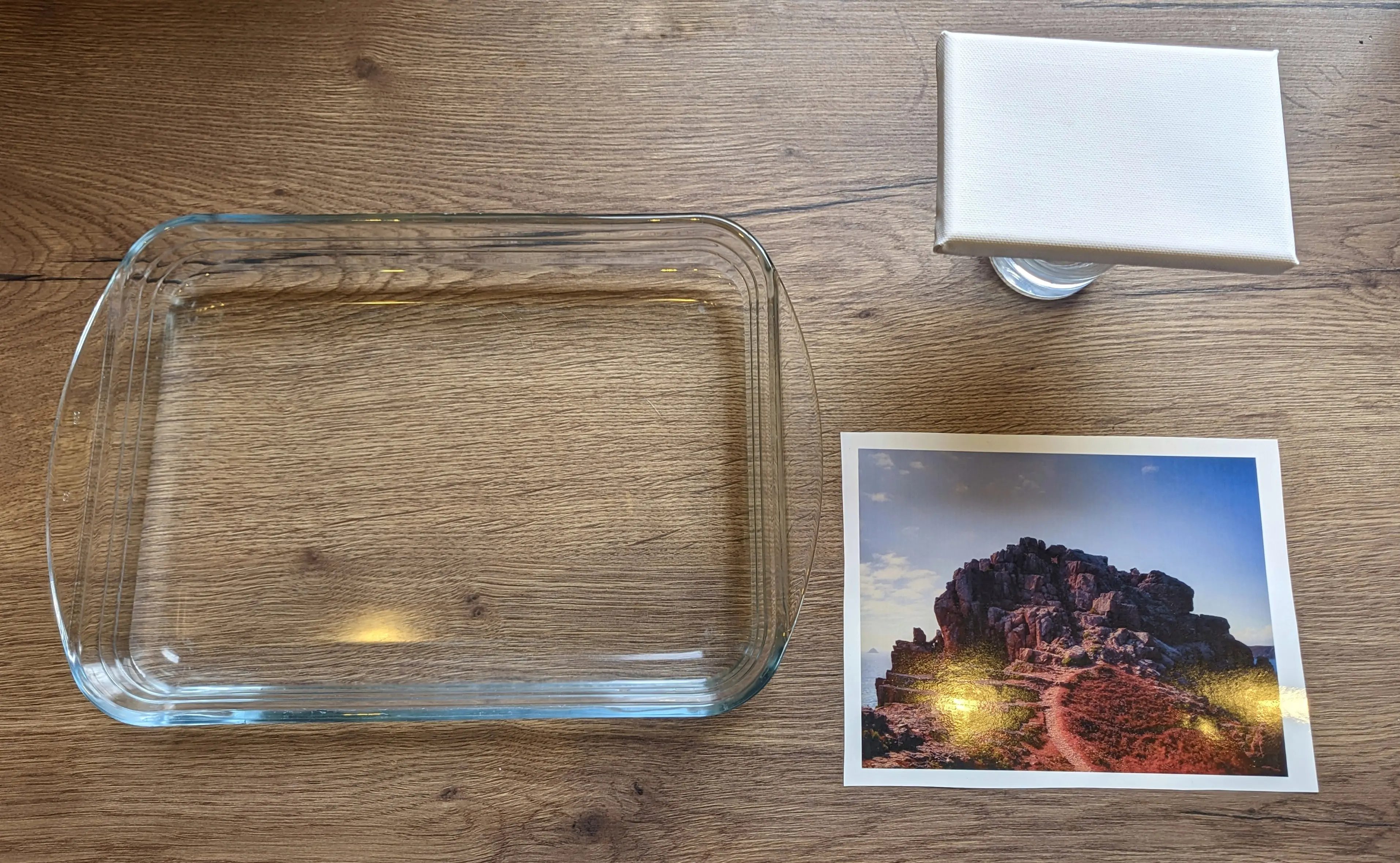 A large glass oven dish filled with water sitting on a kitchen counter, next to the cut out image and the canvas, which has been placed on top of a glass