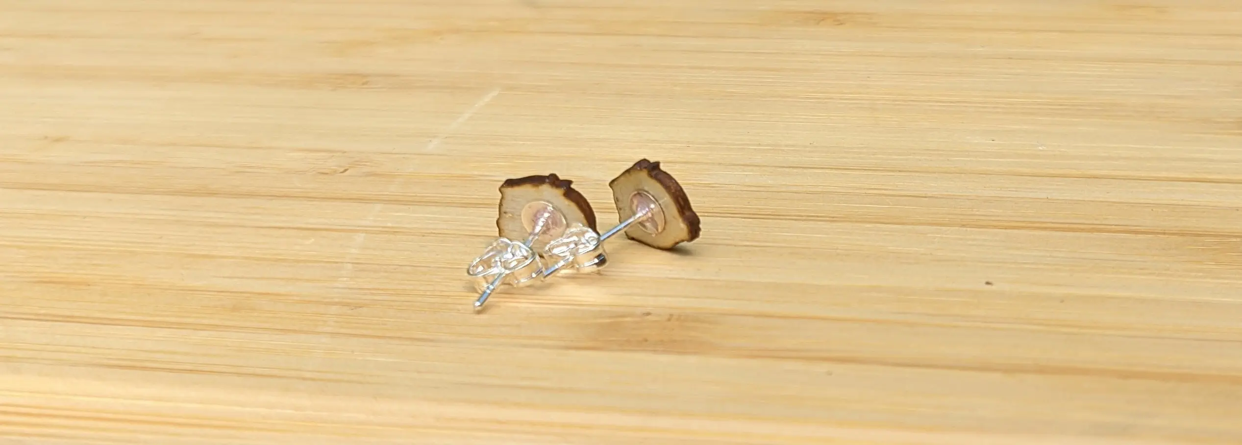 Earring posts stuck to the back of the sloth-shaped wooden pieces. The earring backs have been pushed on the posts.