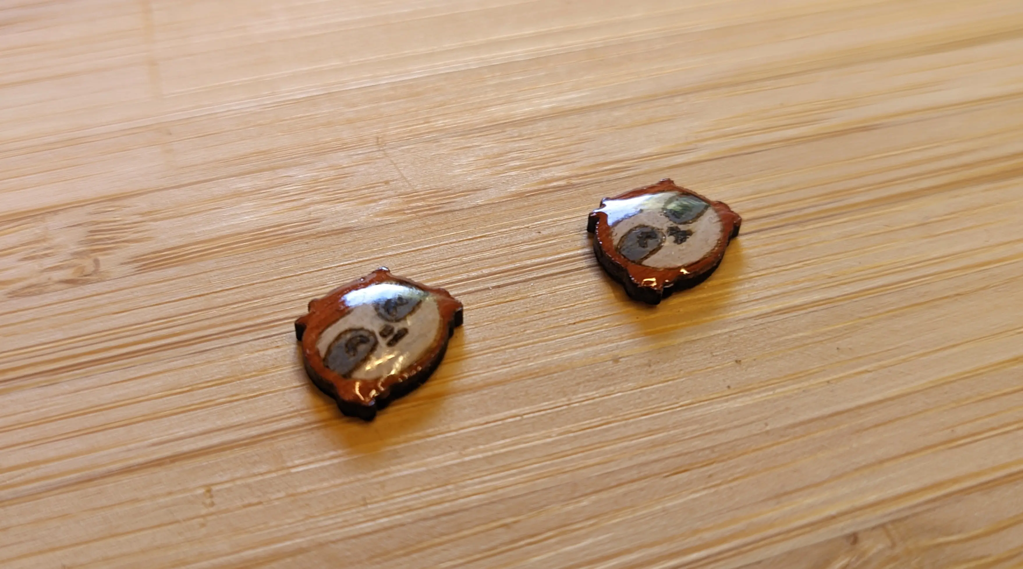 Two painted wooden sloths are lying on the desk. The curve of the resin finish reflects the sunlight. The paint color is more vibrant than before without the resin.