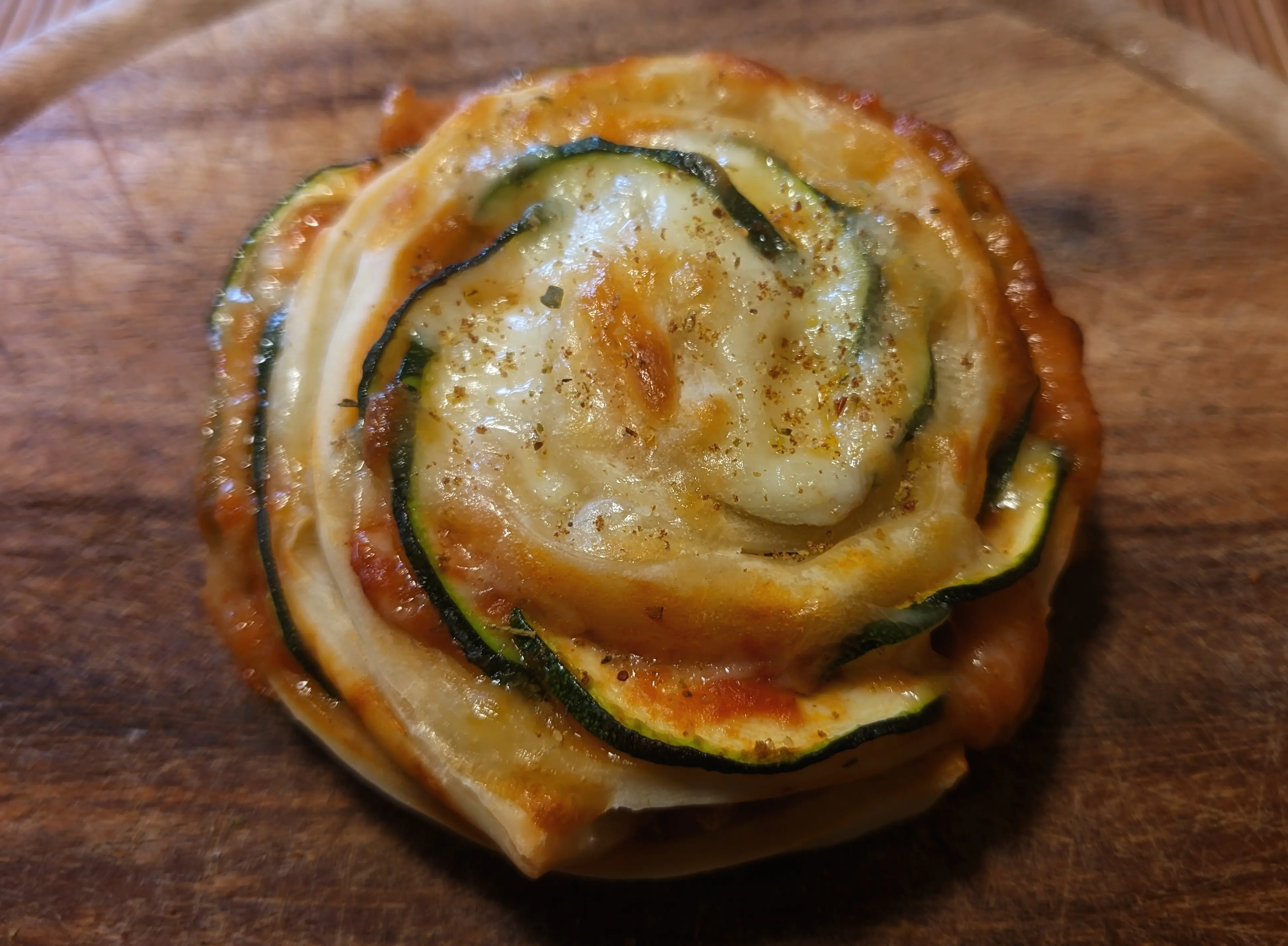 Close-up of a single baked roll, with additional spices on top. The cheese reflects the sunlight.