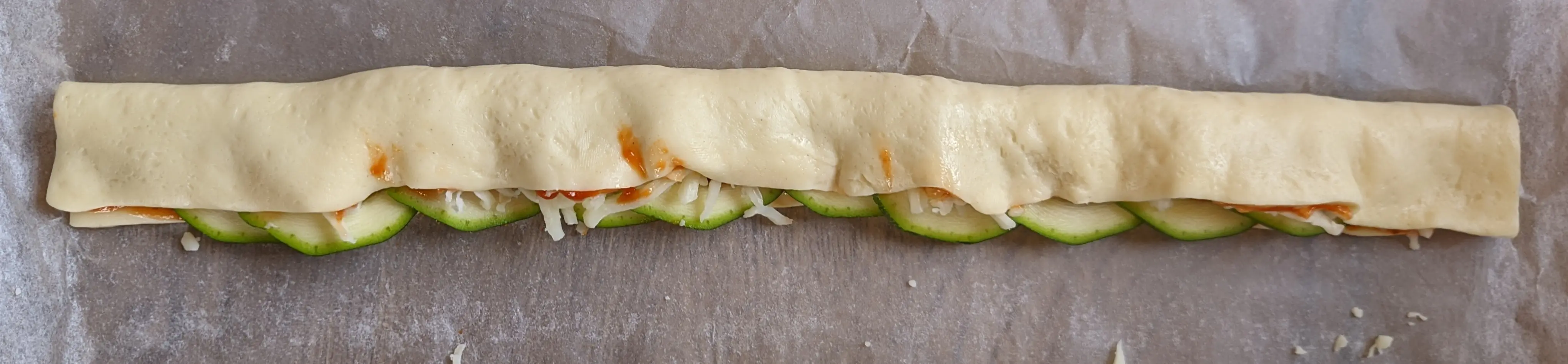 Top-down view showing the left of the dough folded over the zucchini slices.