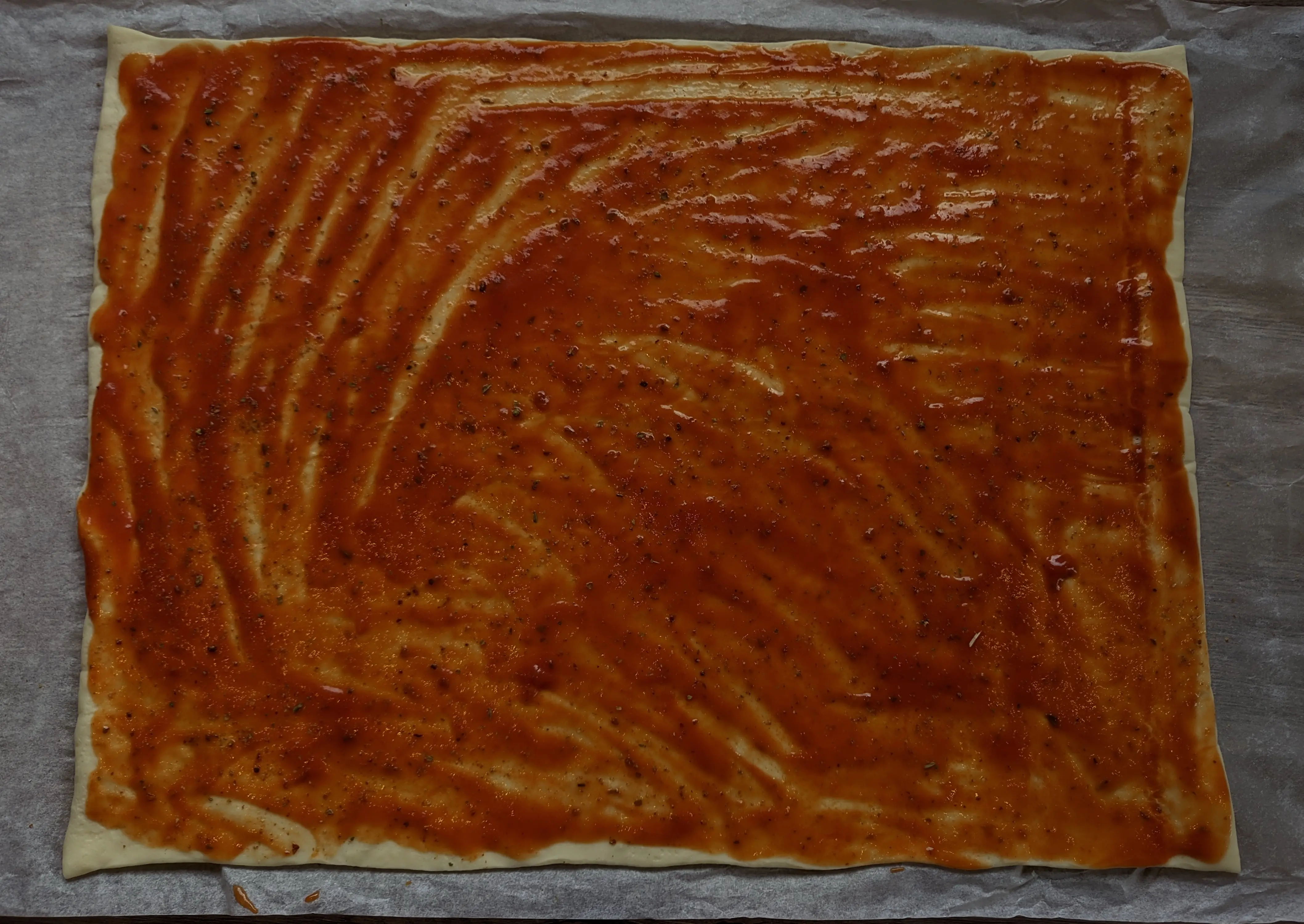 Top-down view of rolled out pizza dough with tomato sauce spread on it.