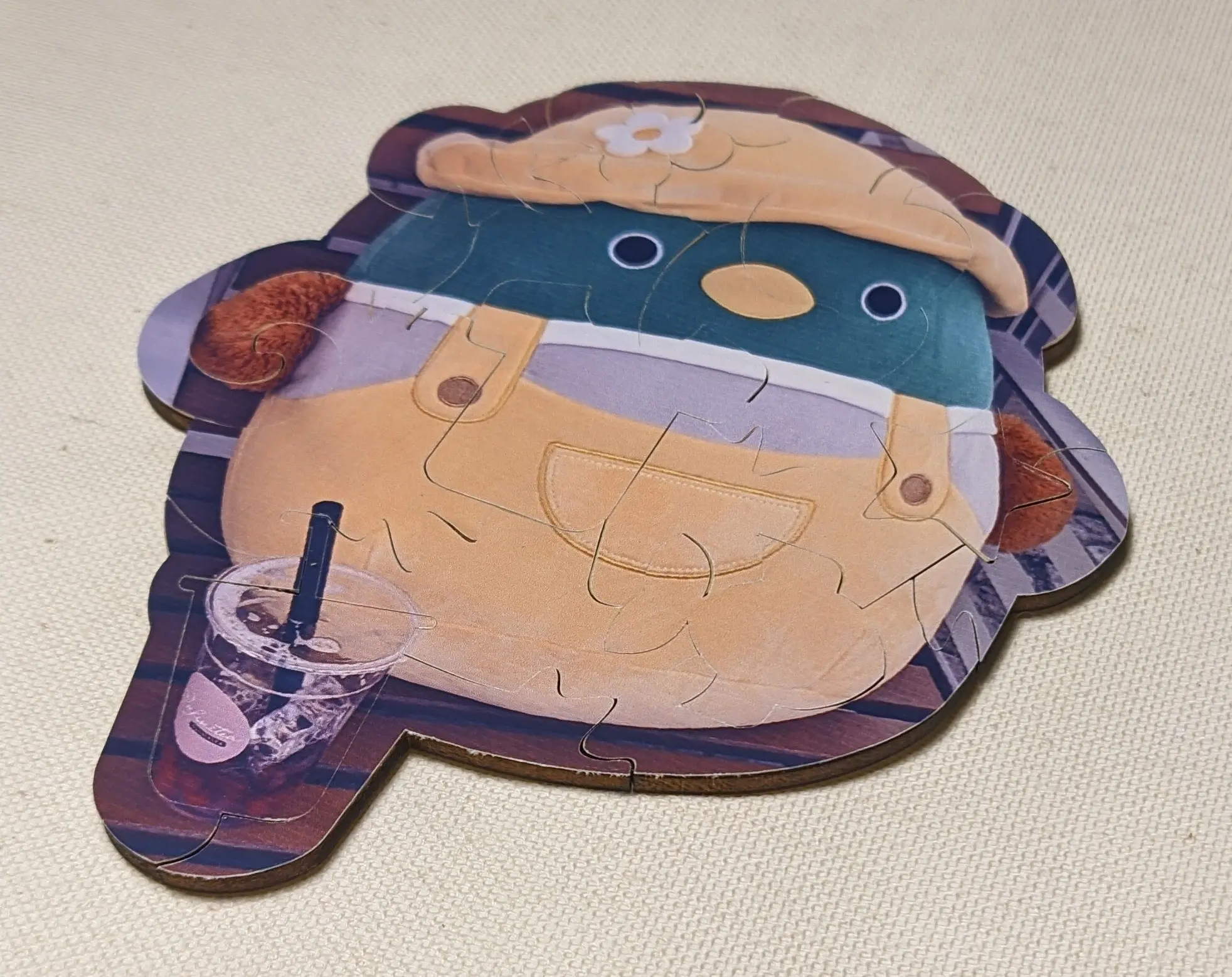 The same wooden puzzle, but all the stickers have been applied to it, revealing a photo of a duck Squishmallow in yellow overalls with a yellow hat sitting on a bench.