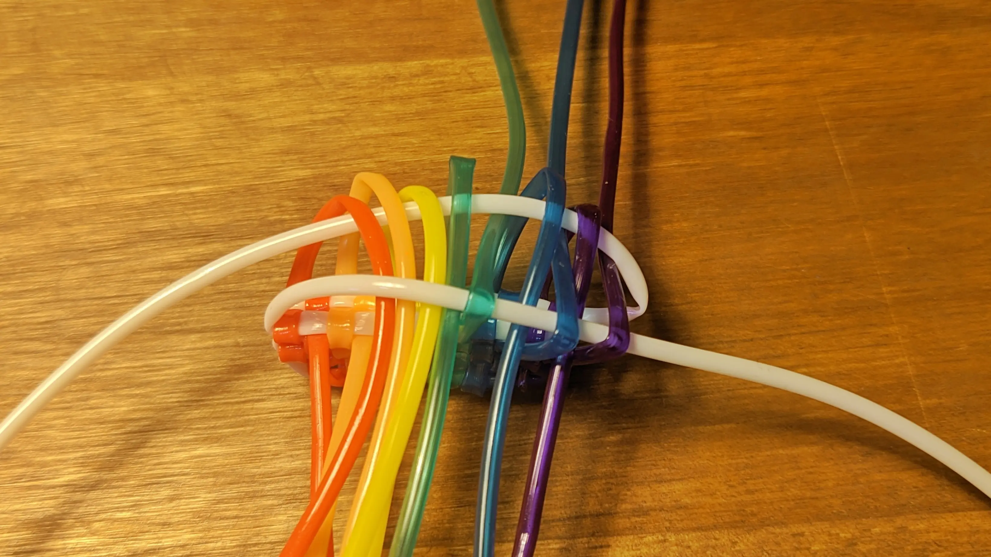 Same knot, but with the lower white strand moved over the upper loops and the lower coloured strands moved over the lower white strand and under the upper white strand in their appropriate columns.