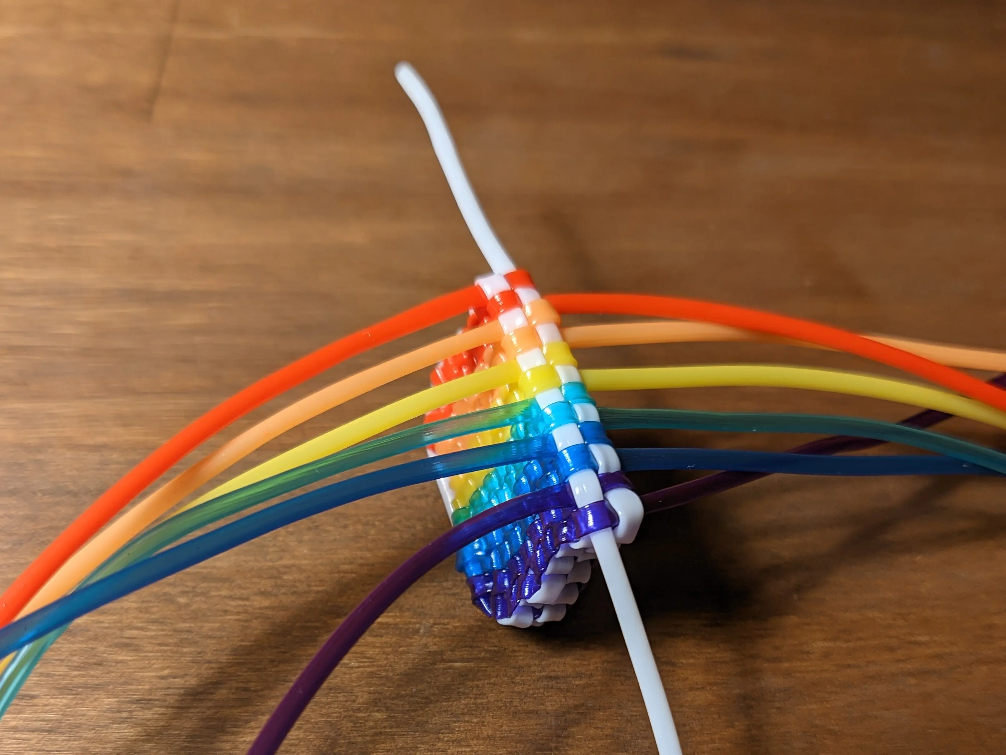 Square flag with strands sticking out placed at an angle on a desk. The coloured strands are still long enough to not fit into the frame. However, the white strands end after just a couple of centimeters.