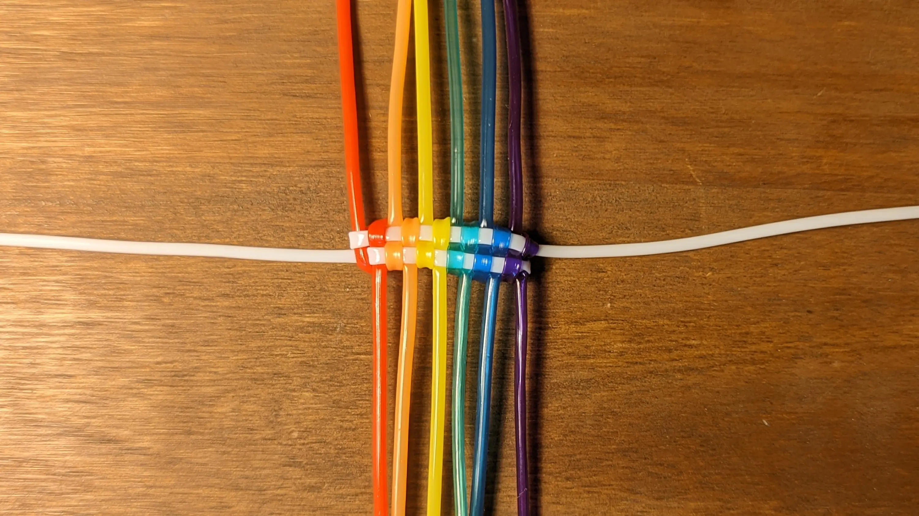 Finished first knot from above; the strands have been pulled tight, making it look like a checkerboard pattern.
Half of the red strand, which used to exit out the bottom, has been folded up and is now going up. The upper half is similarly now exiting the frame at the bottom. The same goes true for the other strands as well.
The strands follow an important order, where the top strands are always left of the corresponding bottom strands.