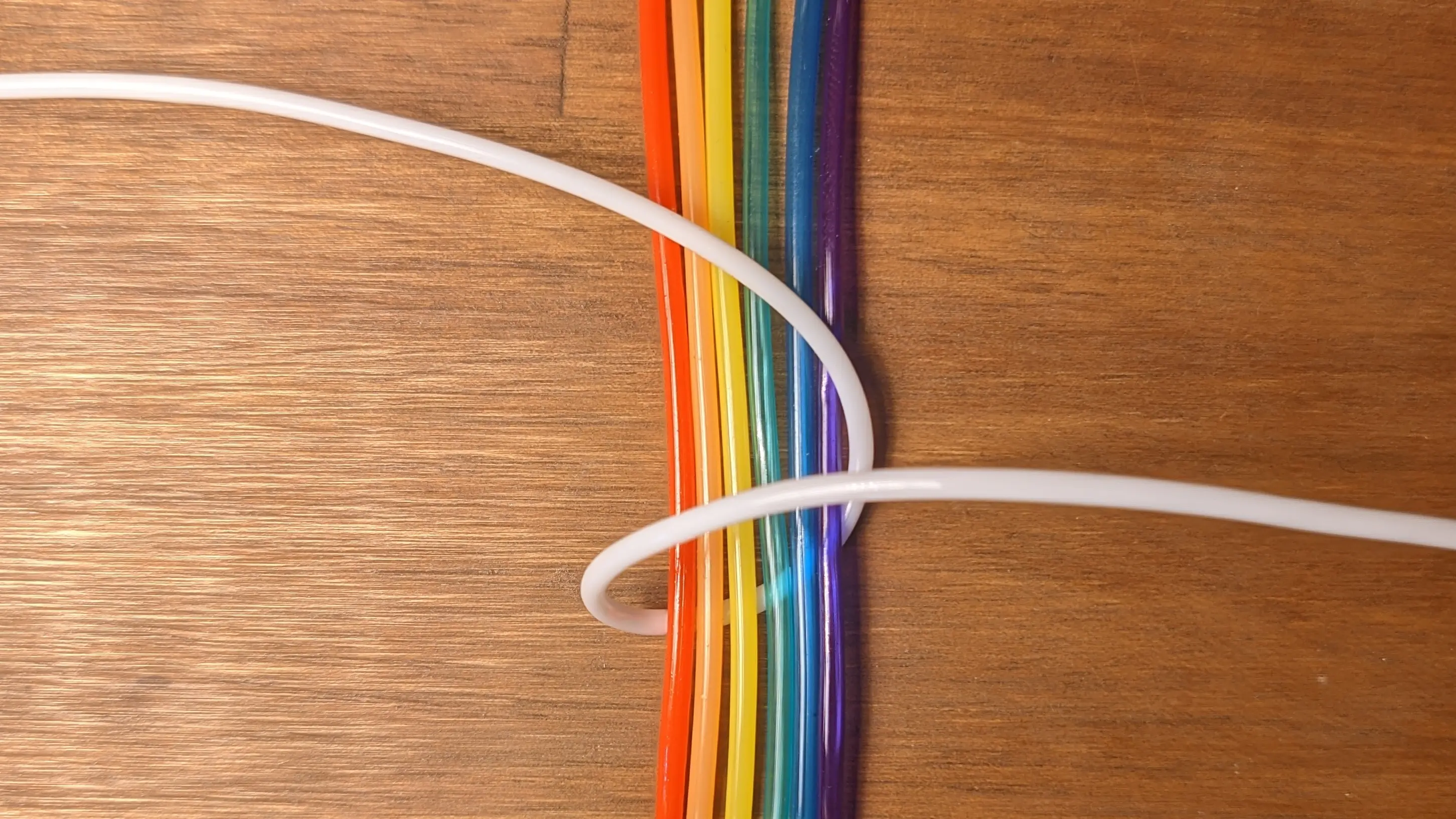 The six rainbow strands placed next to one another above the white strand. One side of them exits the frame at the top and the other side at the bottom. The white strand has been looped over them on either side and is exiting the frame on the left and right.