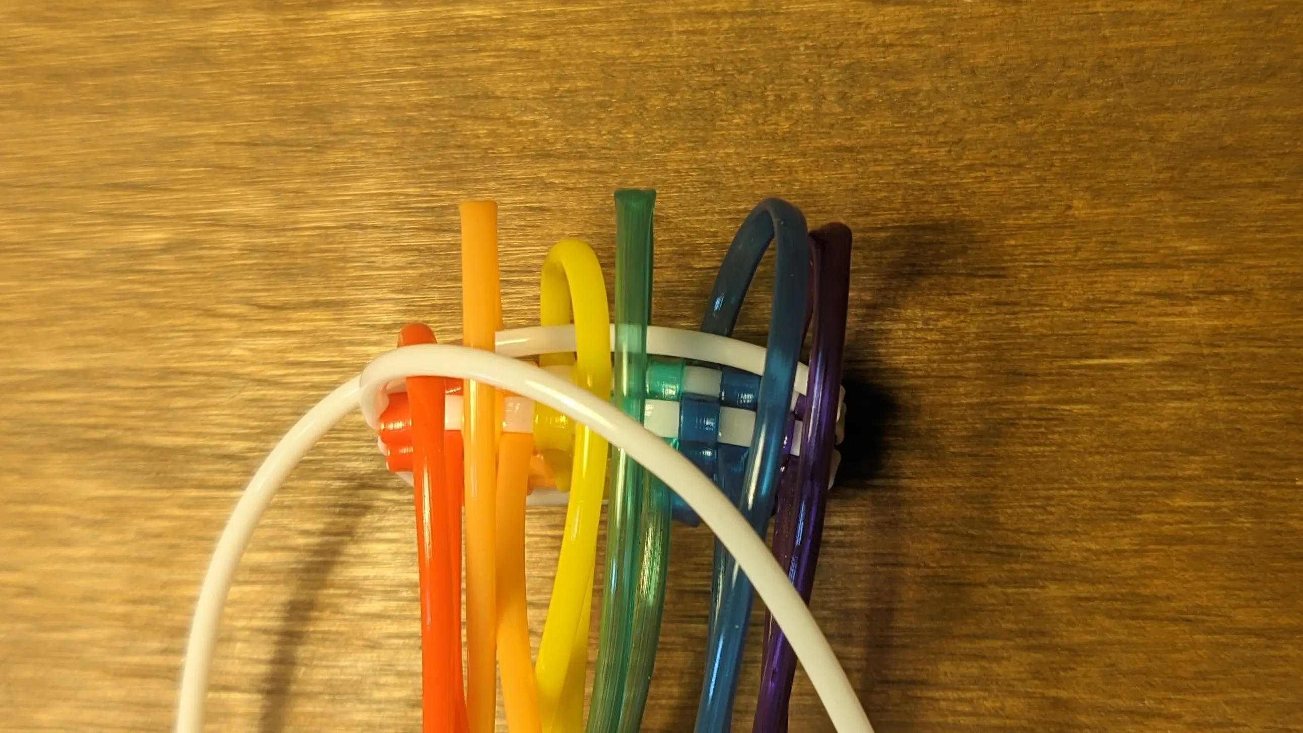 Picture of knots from above; the upper white strand has already been flipped to the opposite site, with the coloured upper strands looping over it. The lower white strand and lower coloured strands are lying randomly.