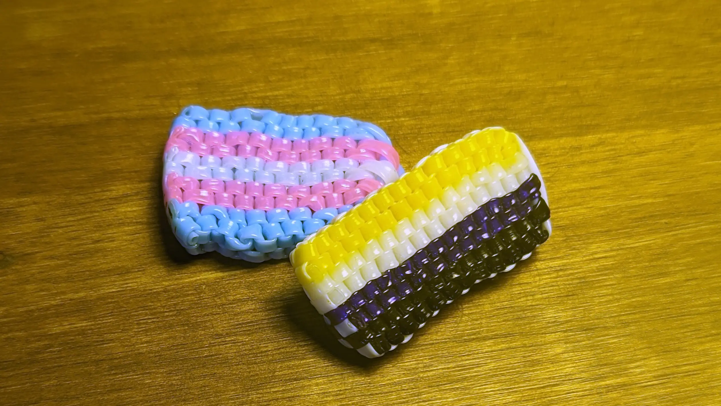 A scoubidou nonbinary-pride flag angled on a scoubidou trans-pride flag.
The nonbinary flag also has a white edge, whereas the trans flag has a blue edge.