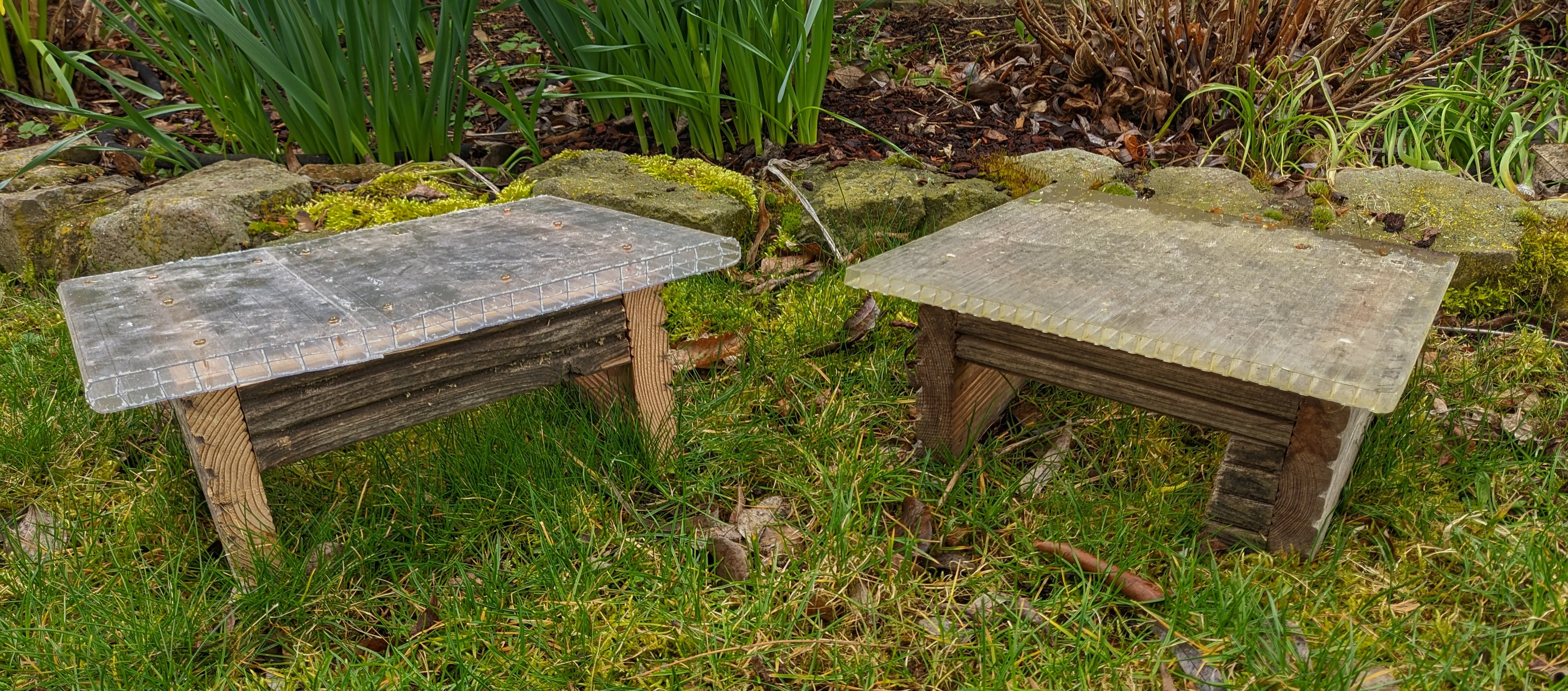 The new hut is sitting left of the old hut in green grass. The new hut is slightly wider than the old one, and the section where the plastic sheet overlaps with itself is barely visible.
