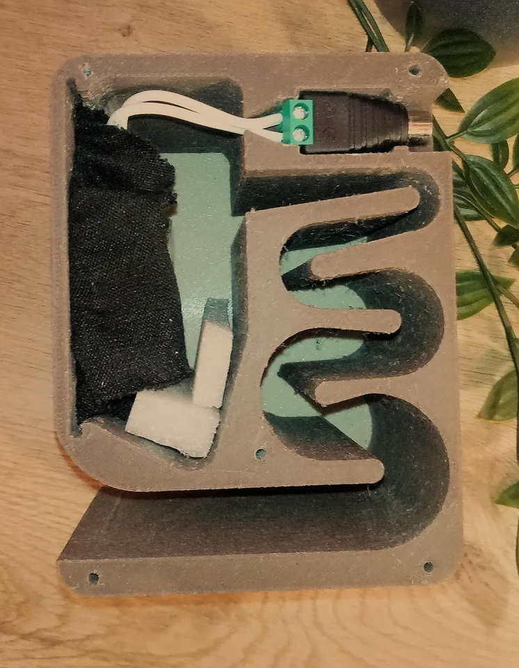 Speaker shown from it&rsquo;s side, with one side panel missing, showing two wires running from the cinch connector to the speaker. You can also see the sound tunnel snaking through the speaker.