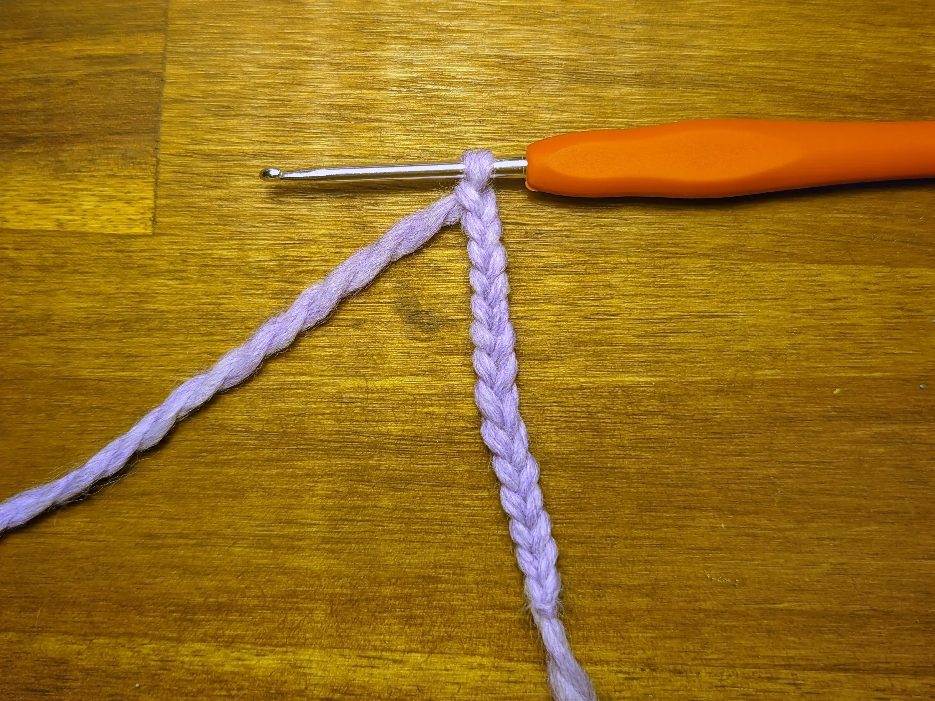 Crochet chain with 13 loops made from lavender yarn dangling from a crochet hook.