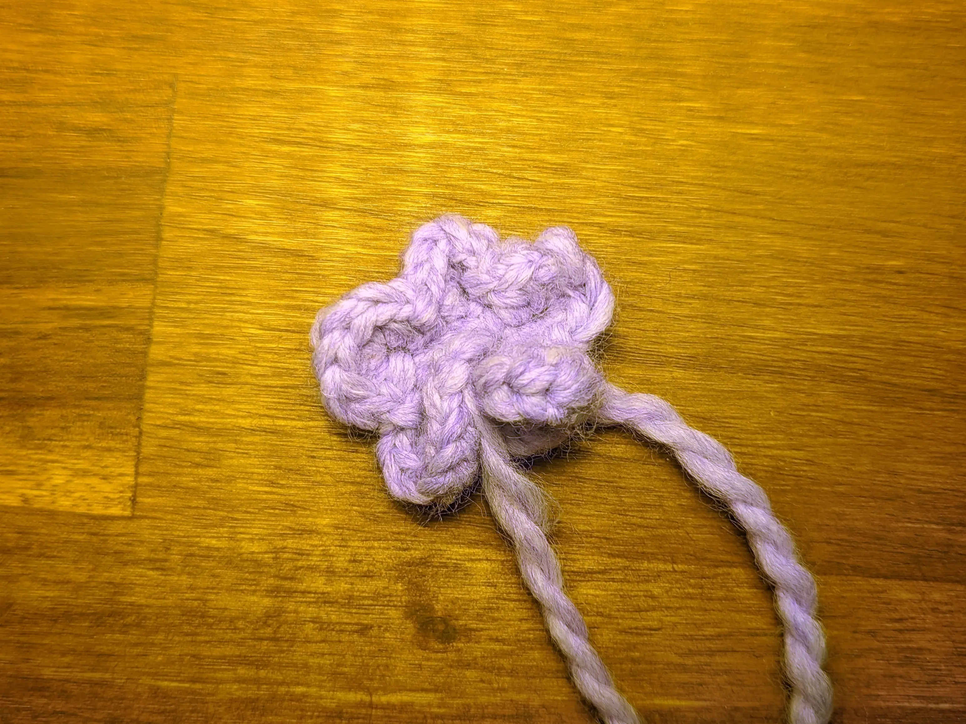 Crochet chain with six lavender petals formed on it. It is curling in on itself, making it look like a simple flower.