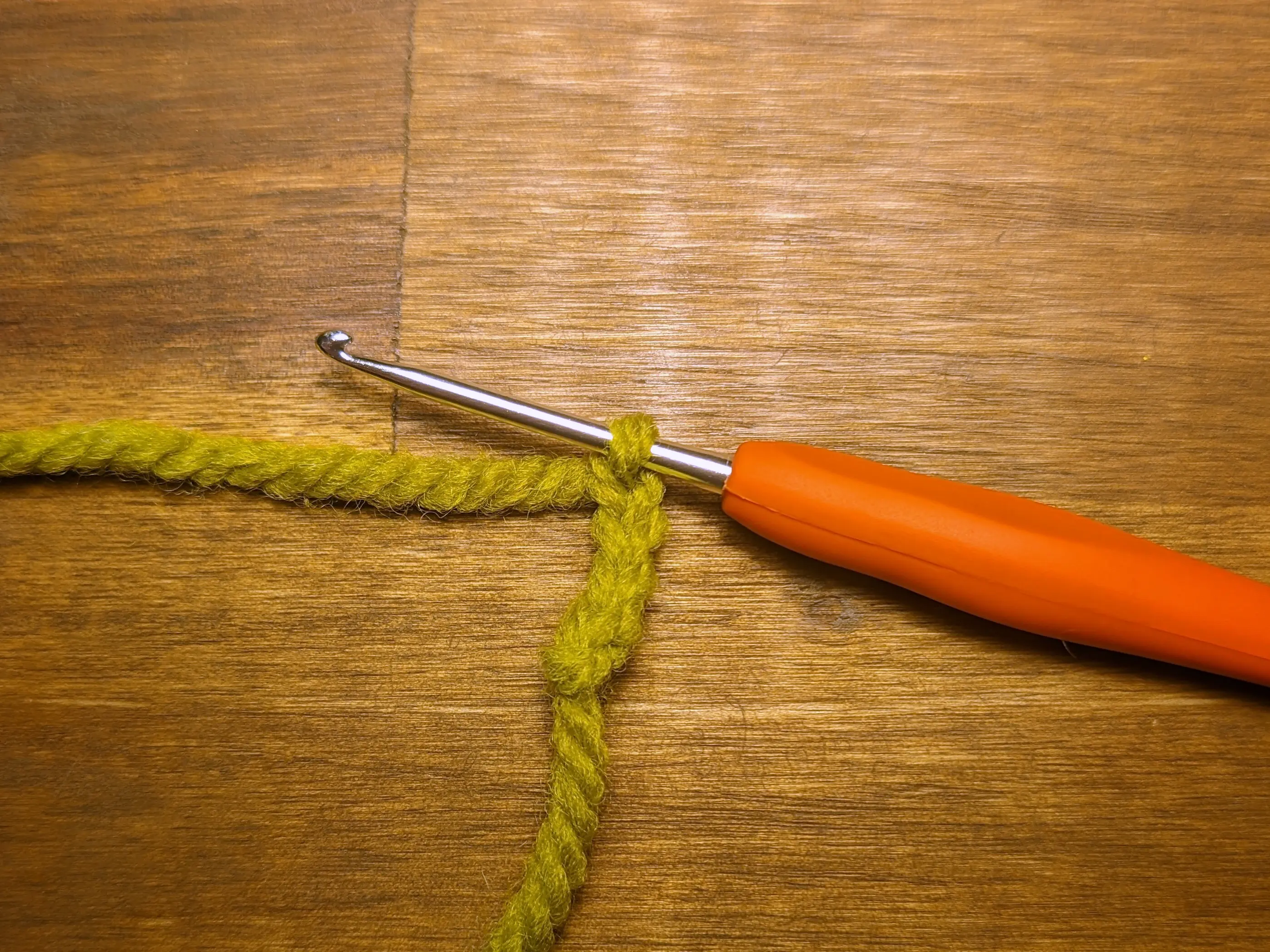 Four crochet chains made from green yarn dangling on a crochet hook.