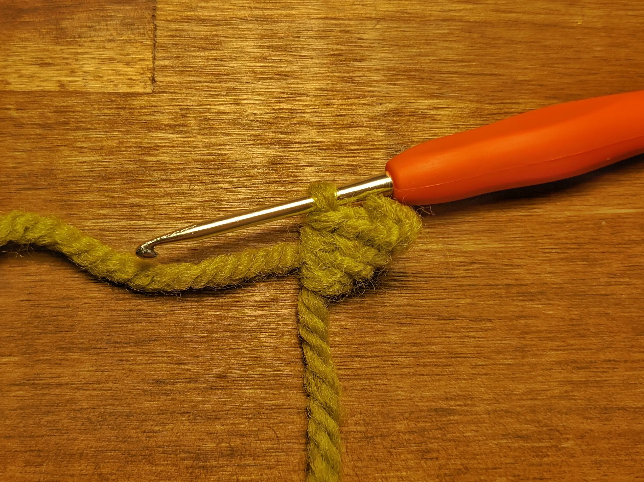 A green triangle-shaped crochet leaf on a crochet hook.